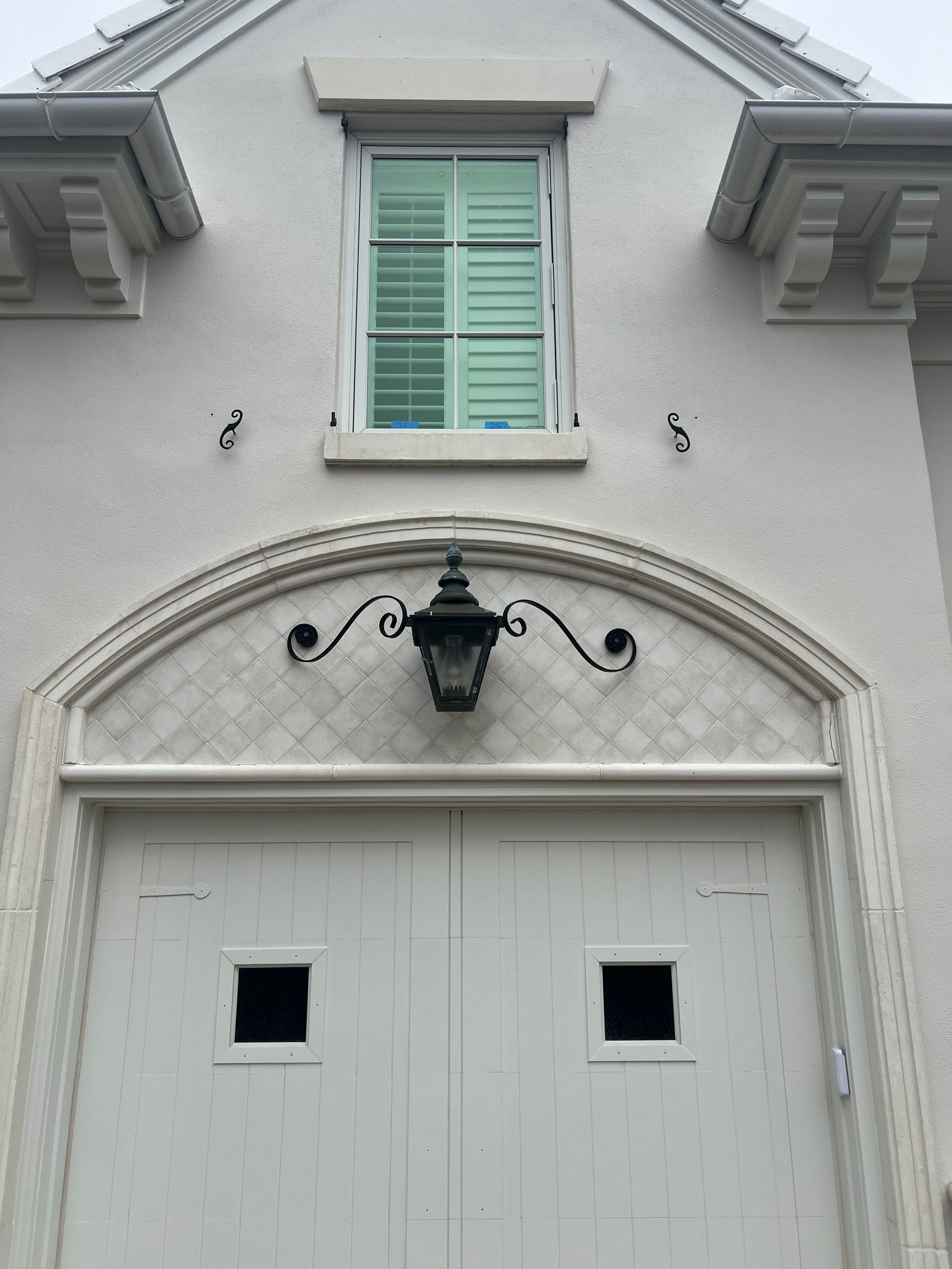 White garage door with arched decorative trim, lamp, and window above.