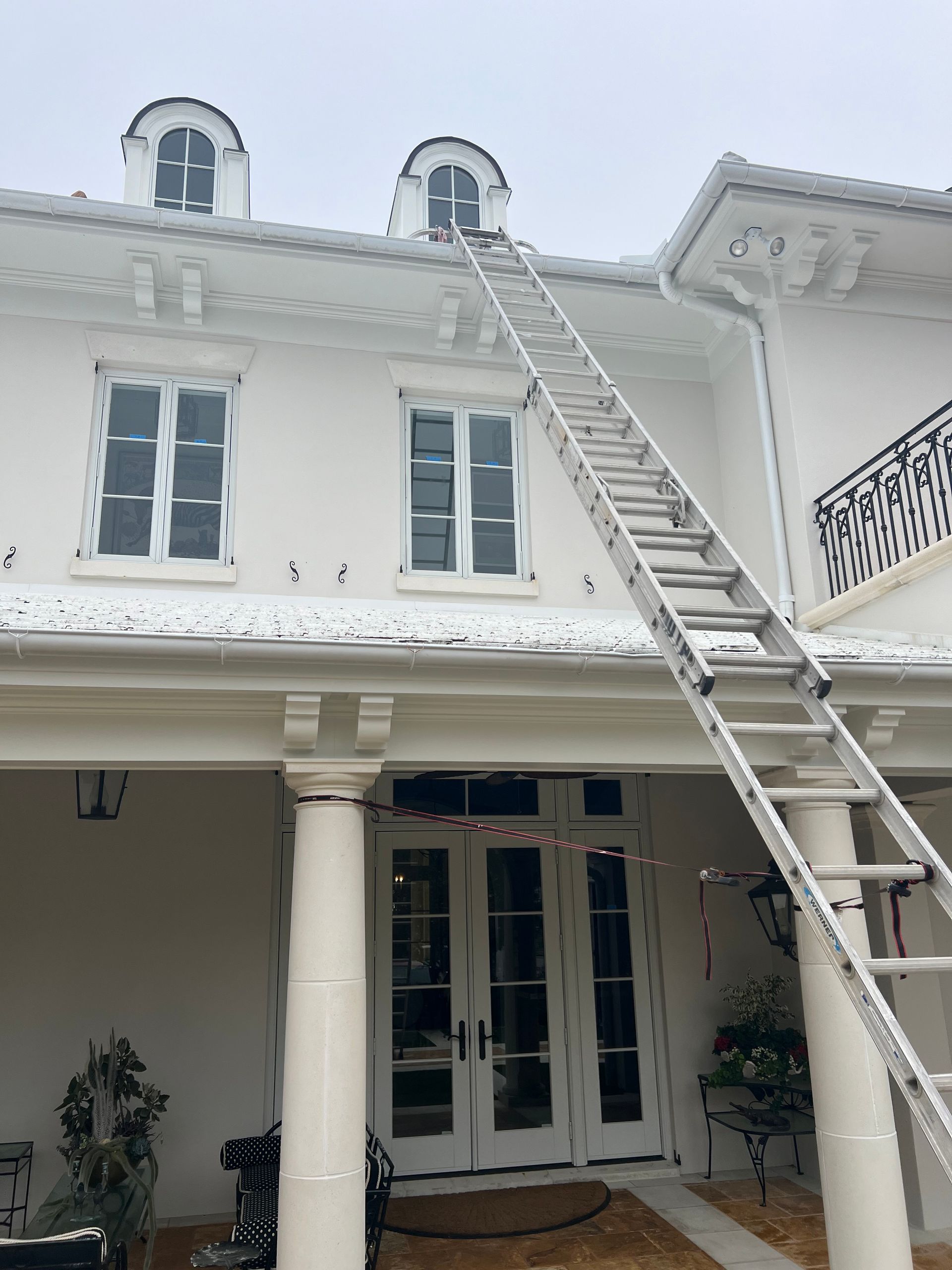 Ladder against white house roof; person potentially working on a gutter.