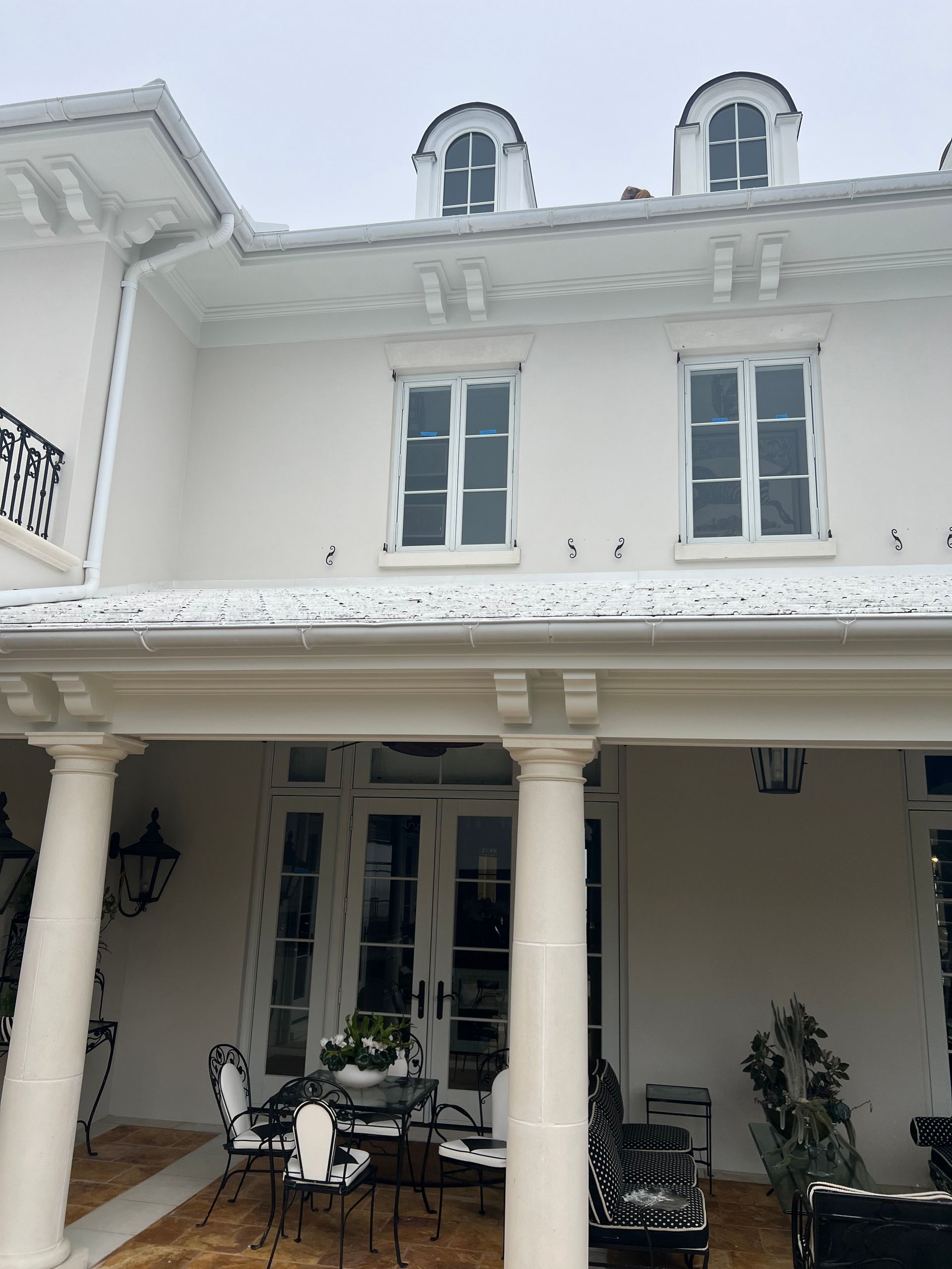 White two-story house with columns, balcony, and covered patio. Cloudy day.