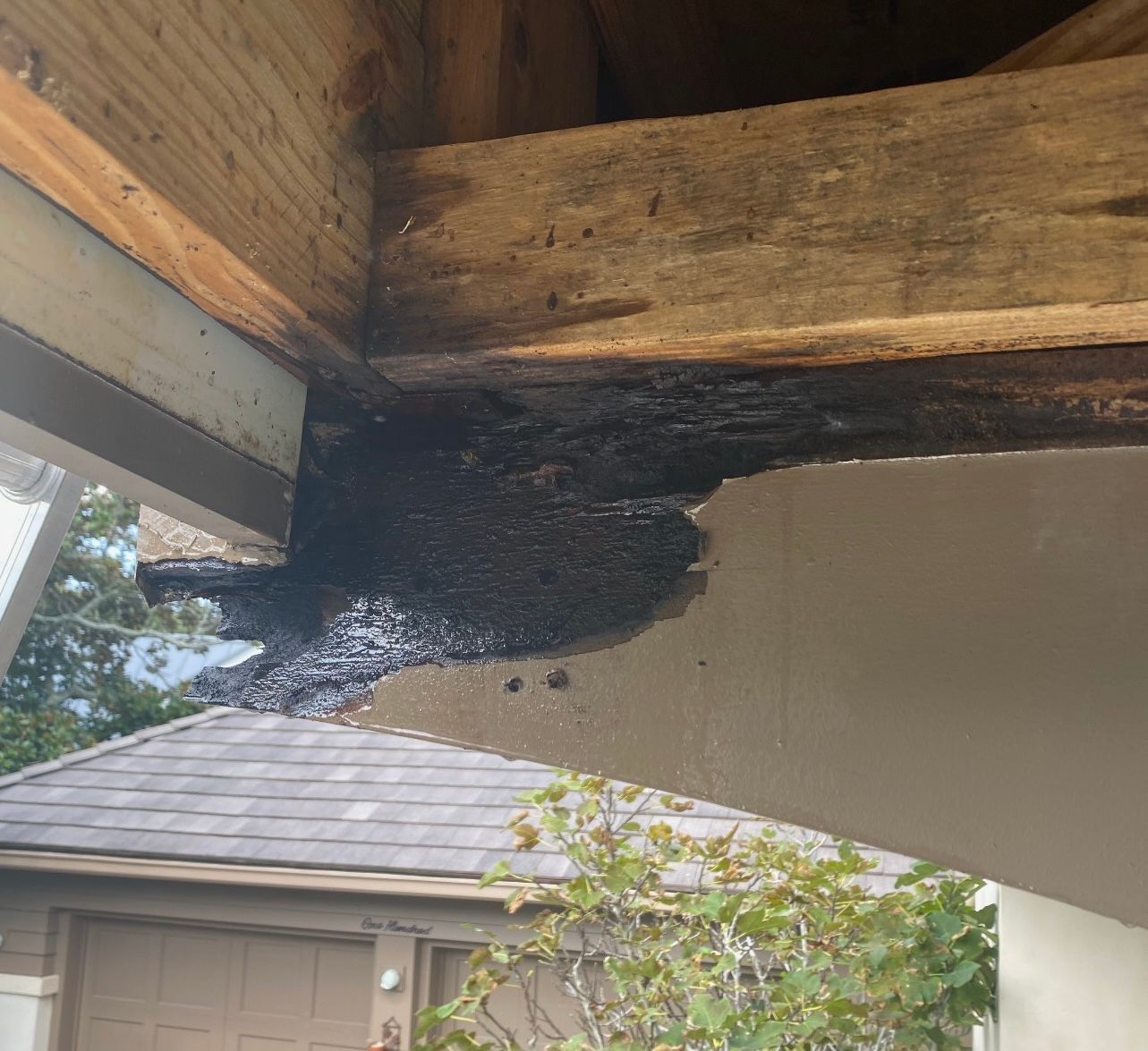 Black tar-like substance dripping from wooden beam and roof eave onto stucco wall.