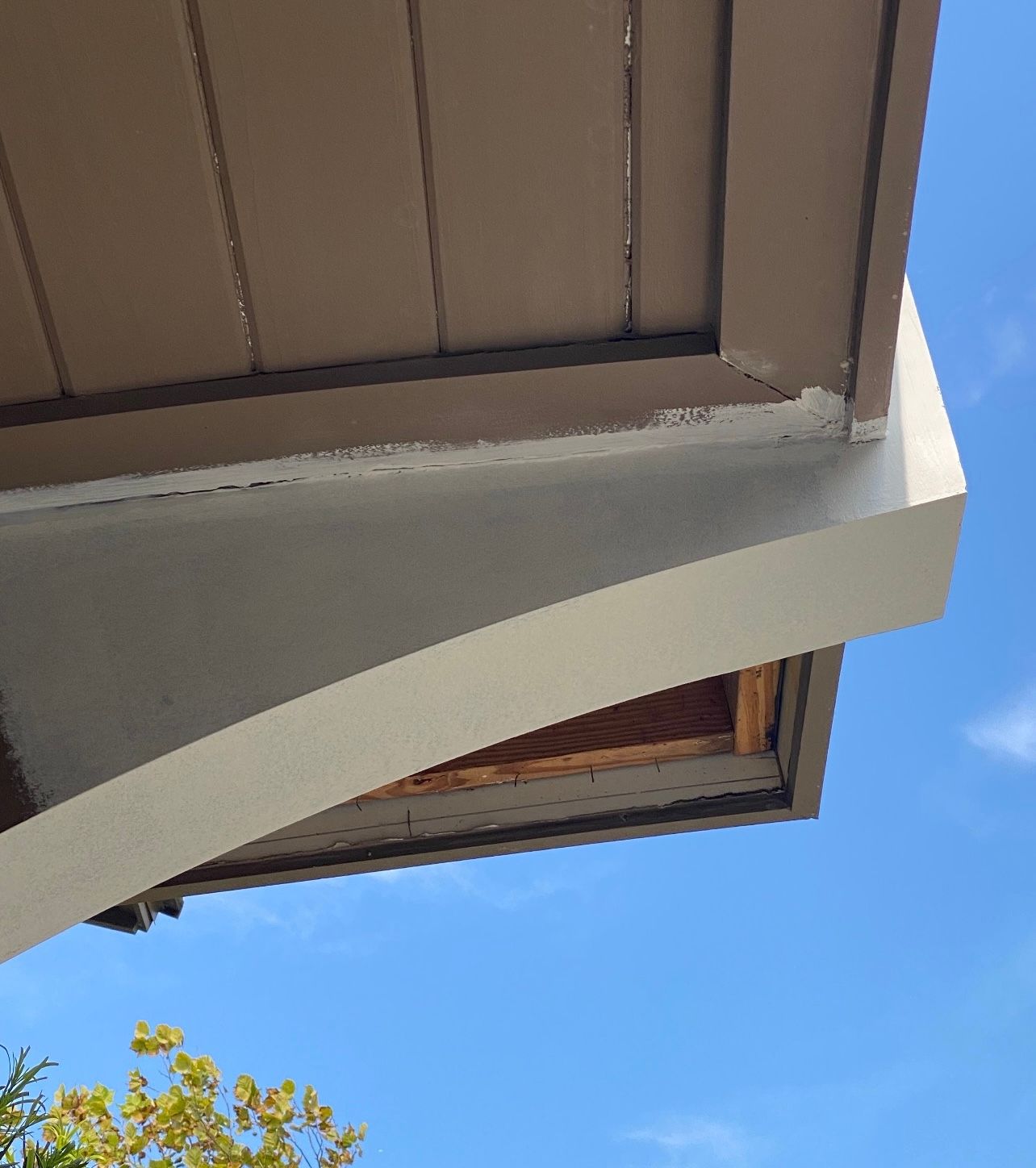 Low-angle view of a light beige curved overhang with a brown underside, against a blue sky.
