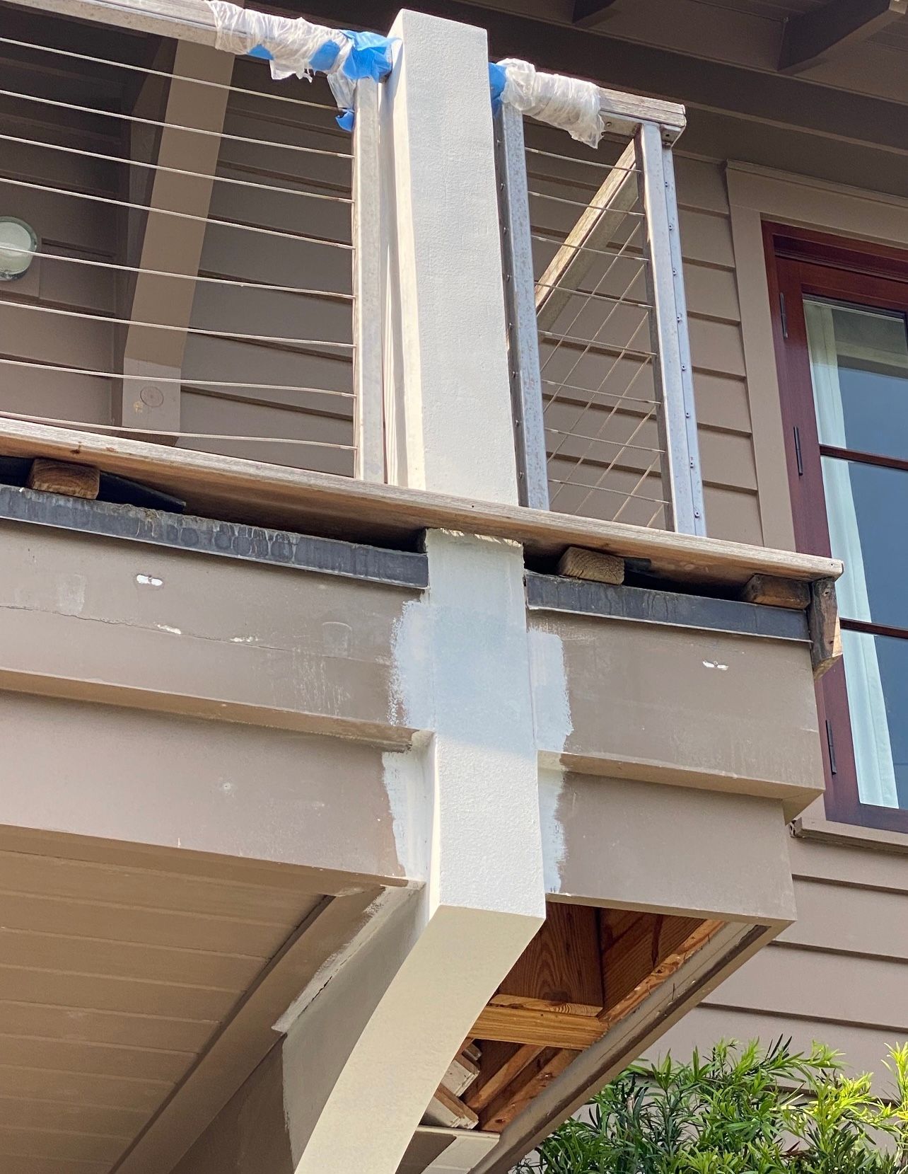 A white-painted support post on a deck, with brown and tan deck boards and a railing with metal cables.