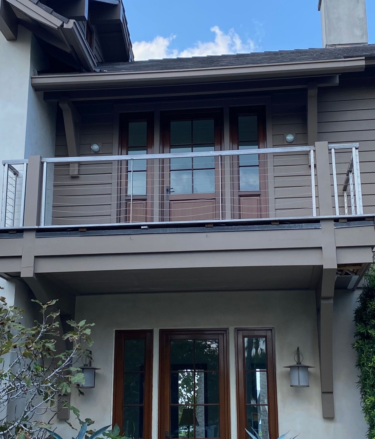 Two-story house with a balcony and brown wooden doors and trim. White railings.