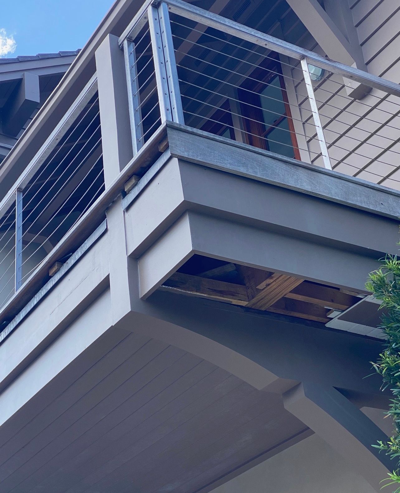 Exterior view of a house with a cable railing balcony, visible wood damage underneath in brown and white colors.