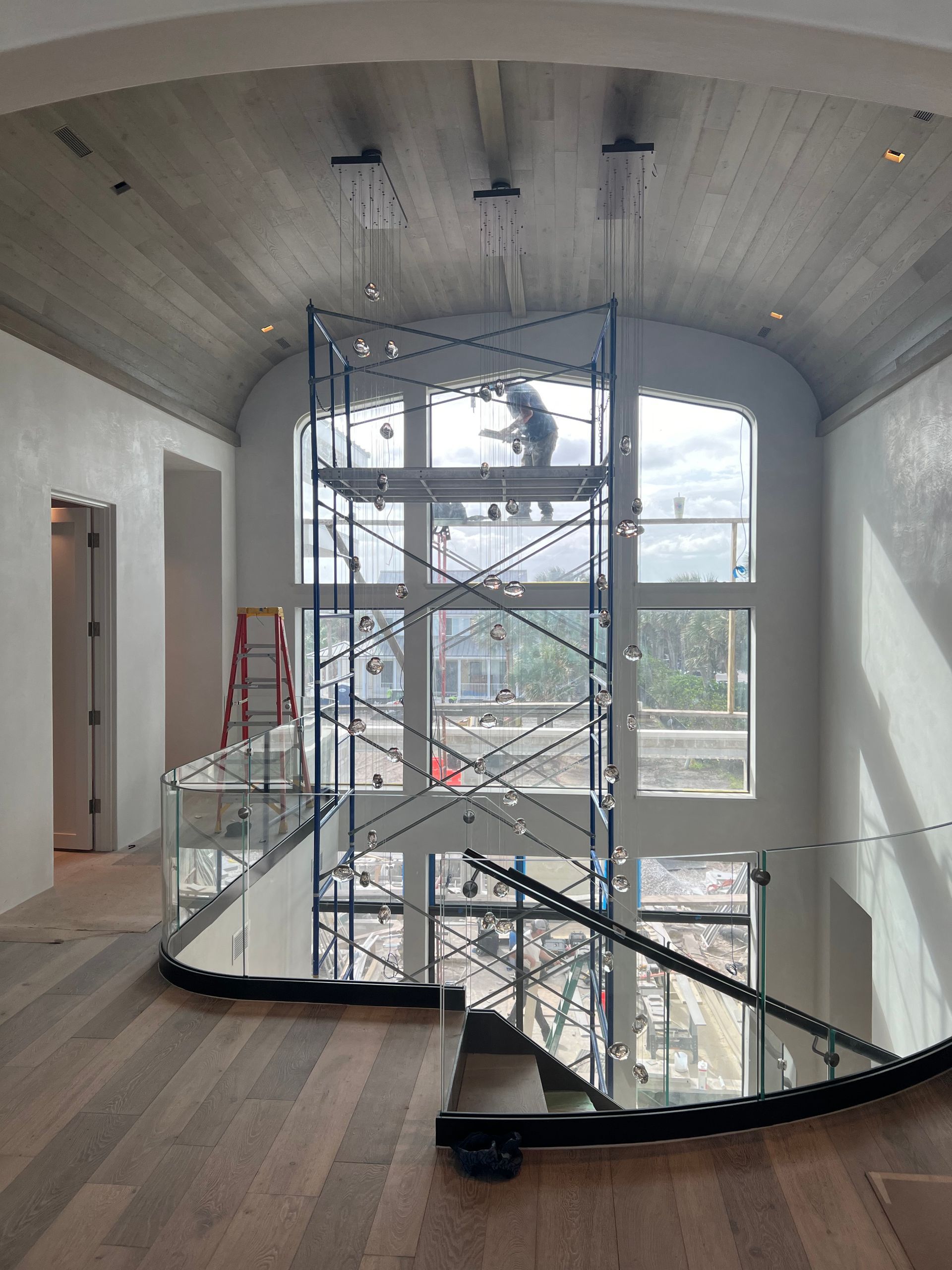 Interior view: Construction worker on scaffolding, tall arched window, staircase with glass railing.
