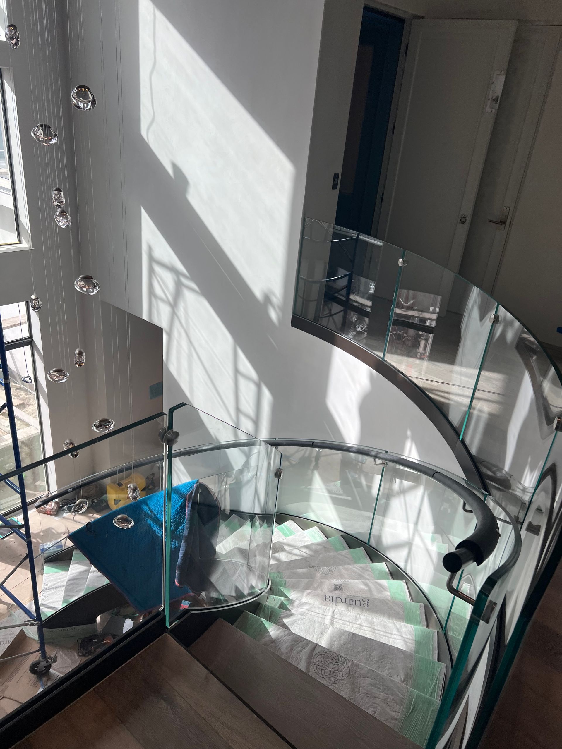 Curved glass staircase with wooden steps, metal railings, and natural light.