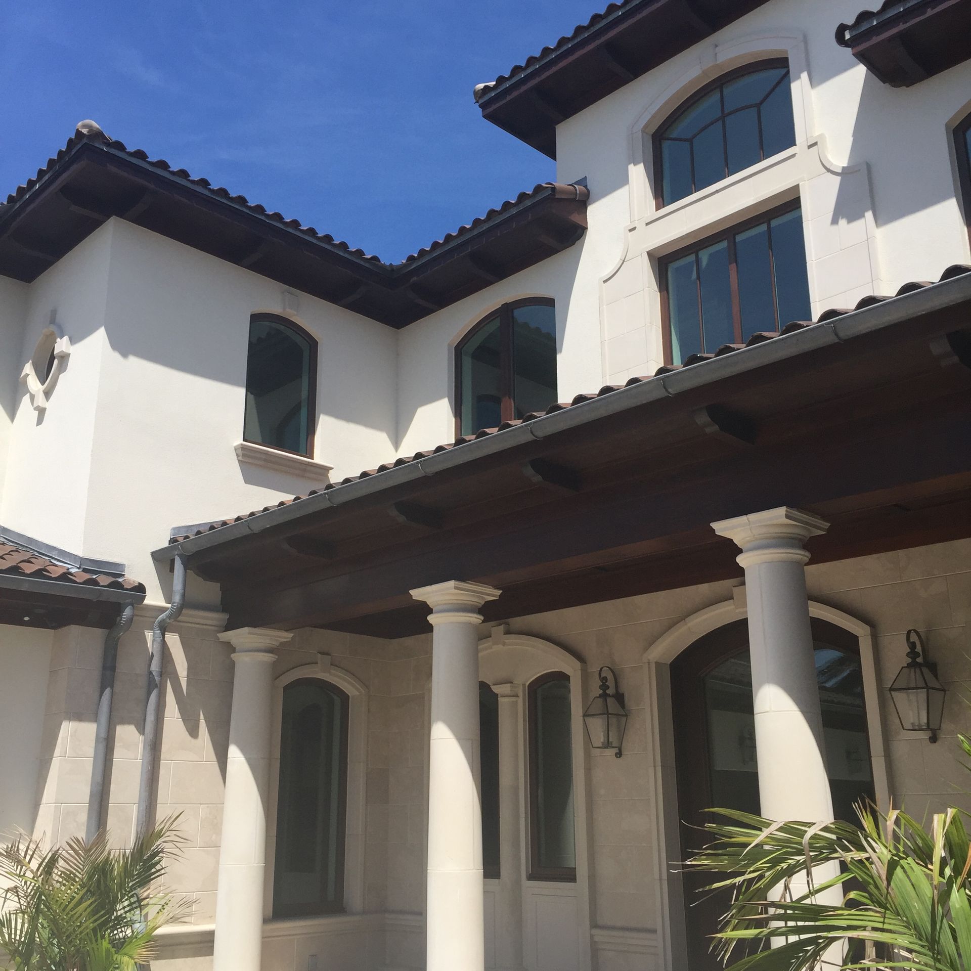 Exterior of a two-story home with white stucco walls, dark wood accents, arched windows, and columns.