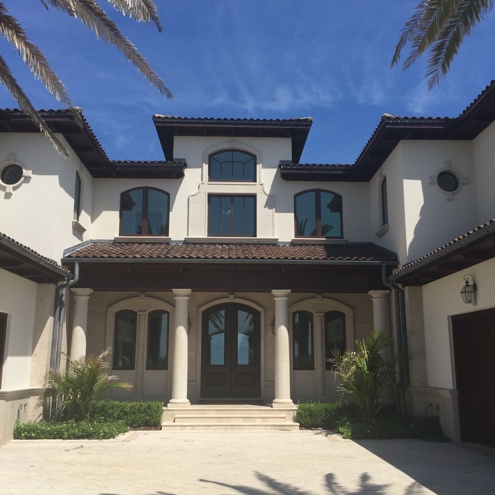 Elegant white stucco home with brown accents, blue sky, and palm fronds.