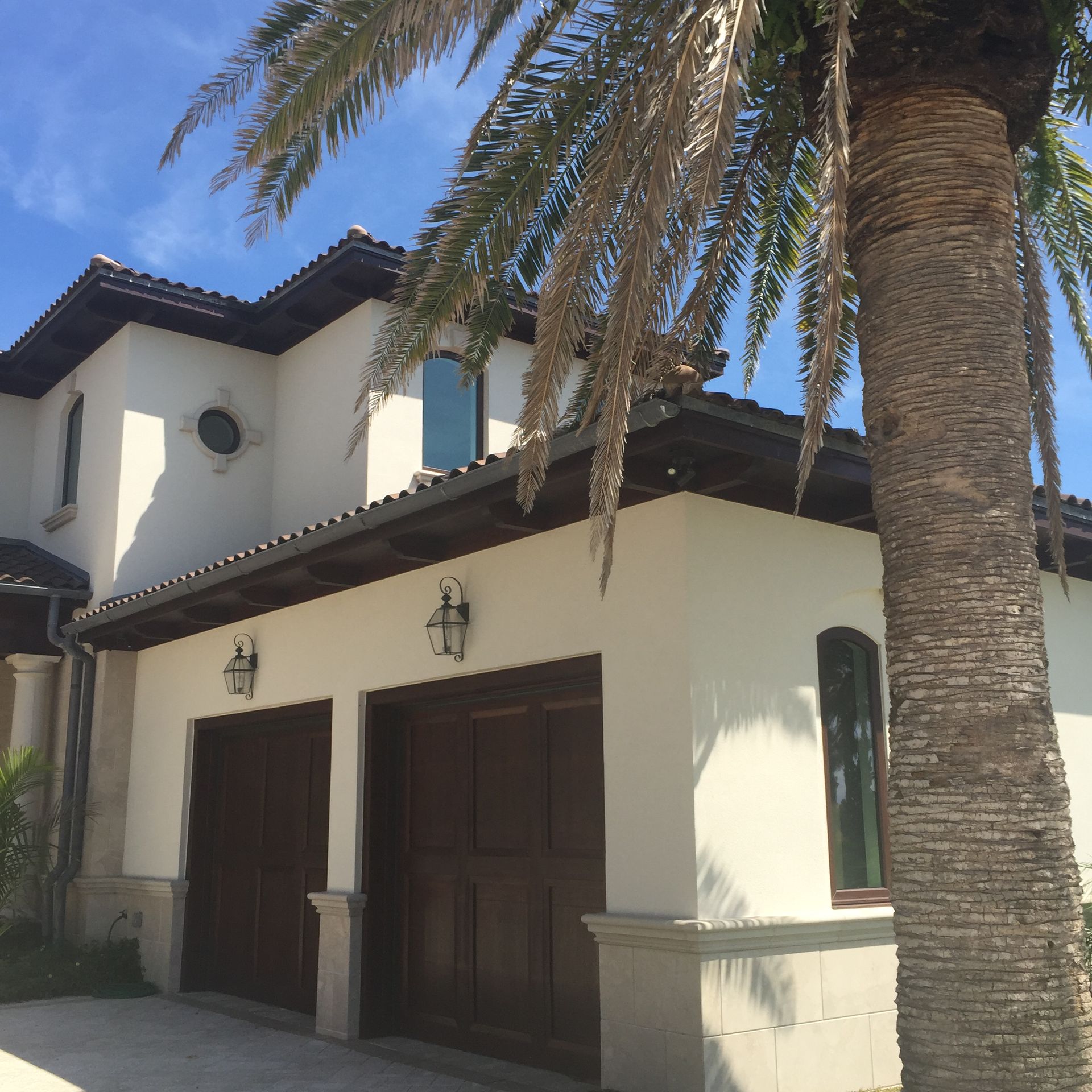 White stucco house with brown garage doors, palm tree in front, blue sky.