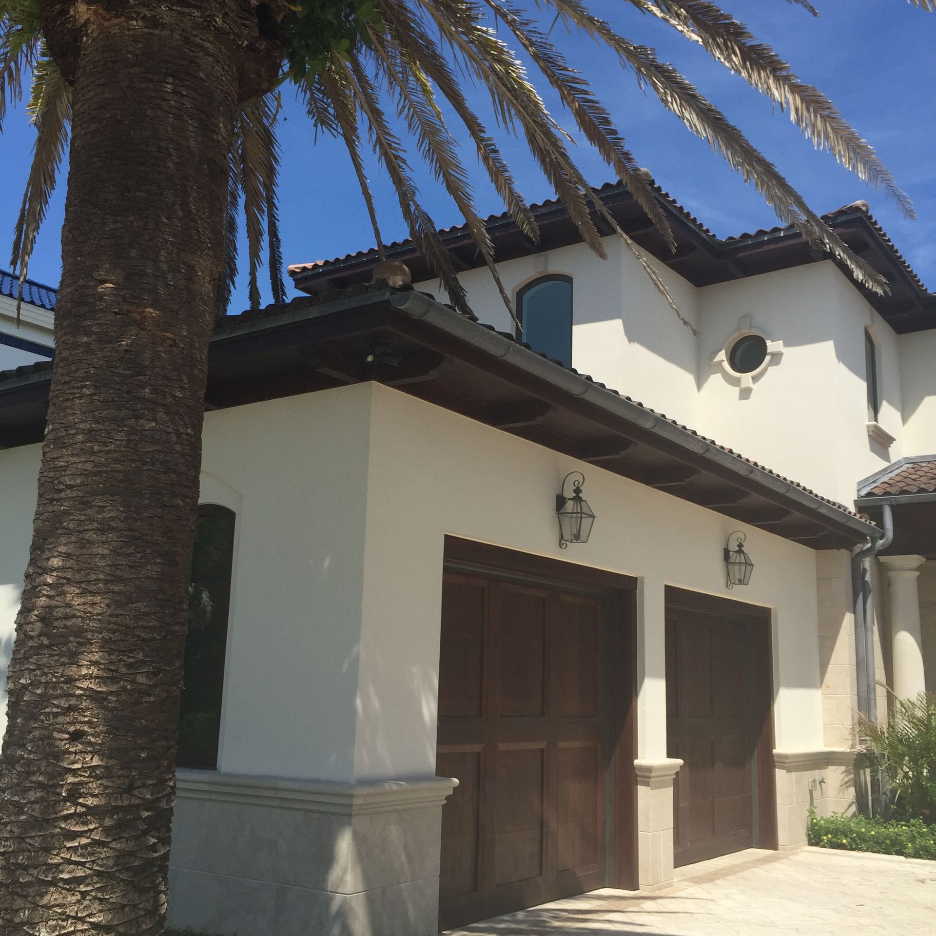 White stucco house with brown garage doors, palm tree, and blue sky.