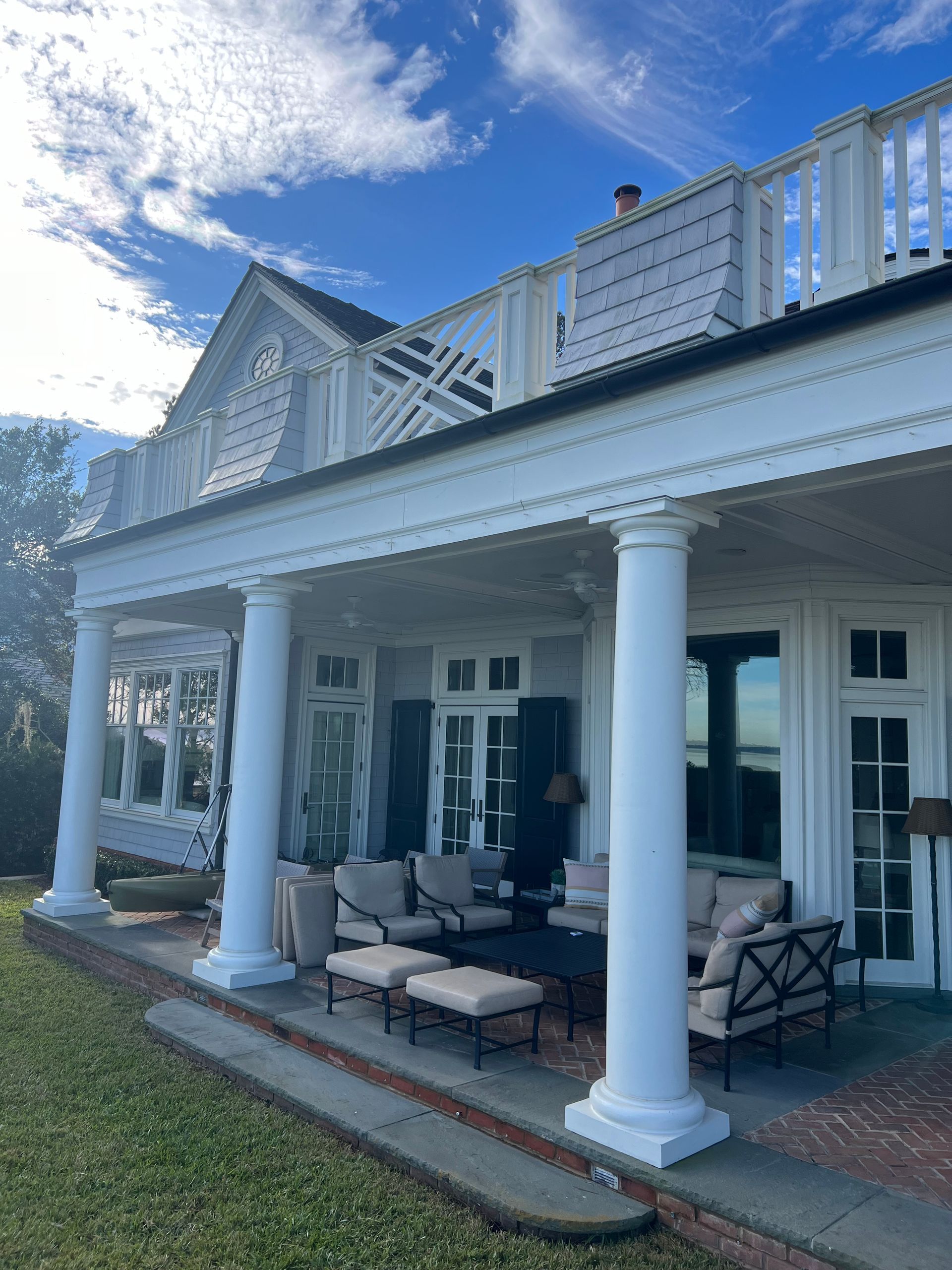 White porch with columns, outdoor furniture, and ocean view, under a blue sky.