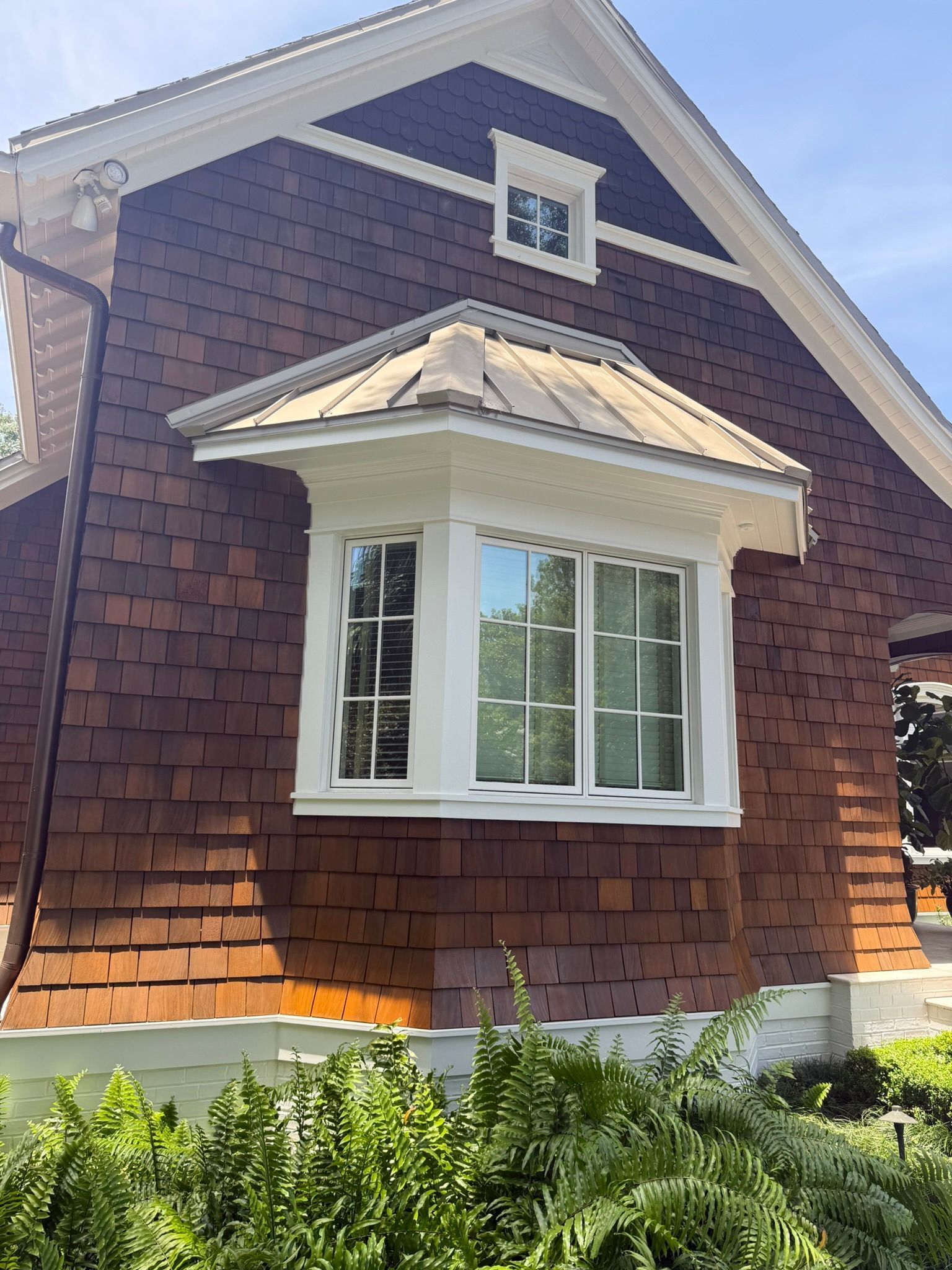 Brown shingle-sided house with a white-framed bay window and small window in the gable.