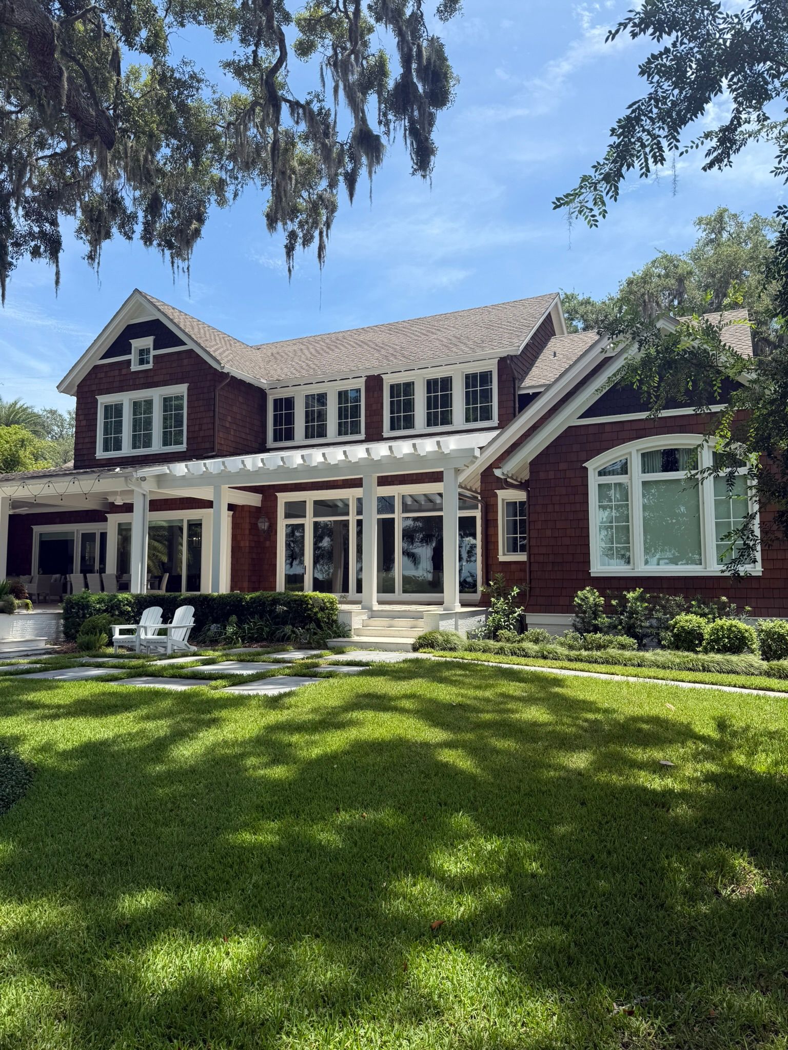 Brick house with white columns, windows, and a green lawn under a sunny sky.