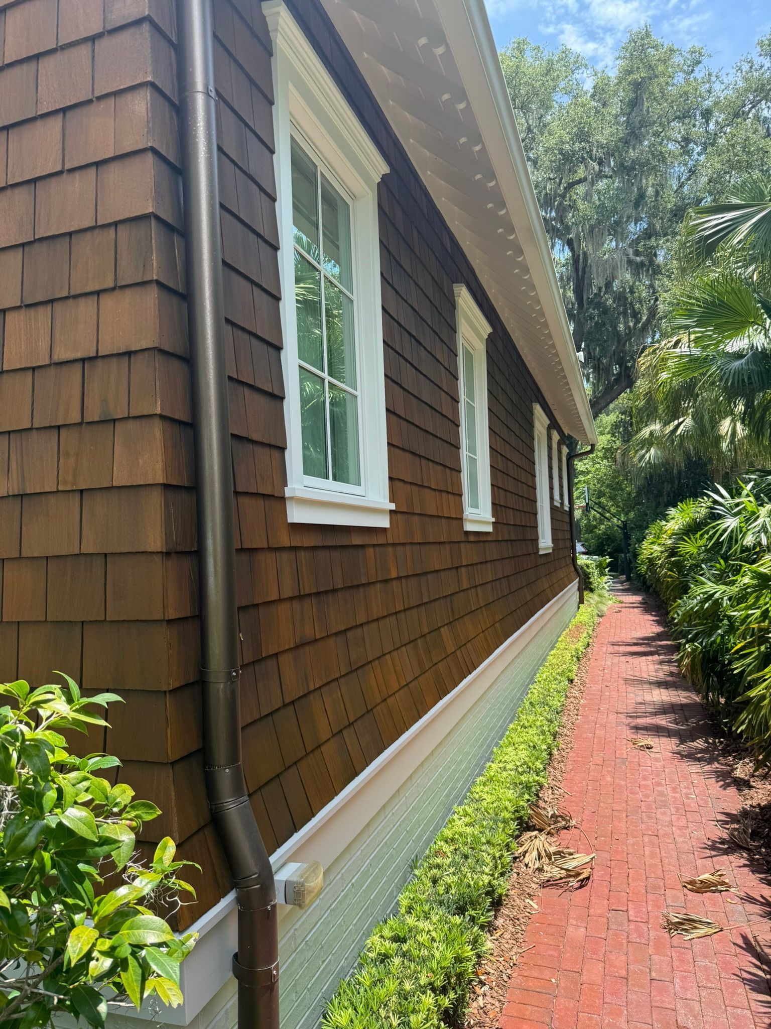 Brown shingle siding on a building with white-framed windows. A brick path runs alongside.