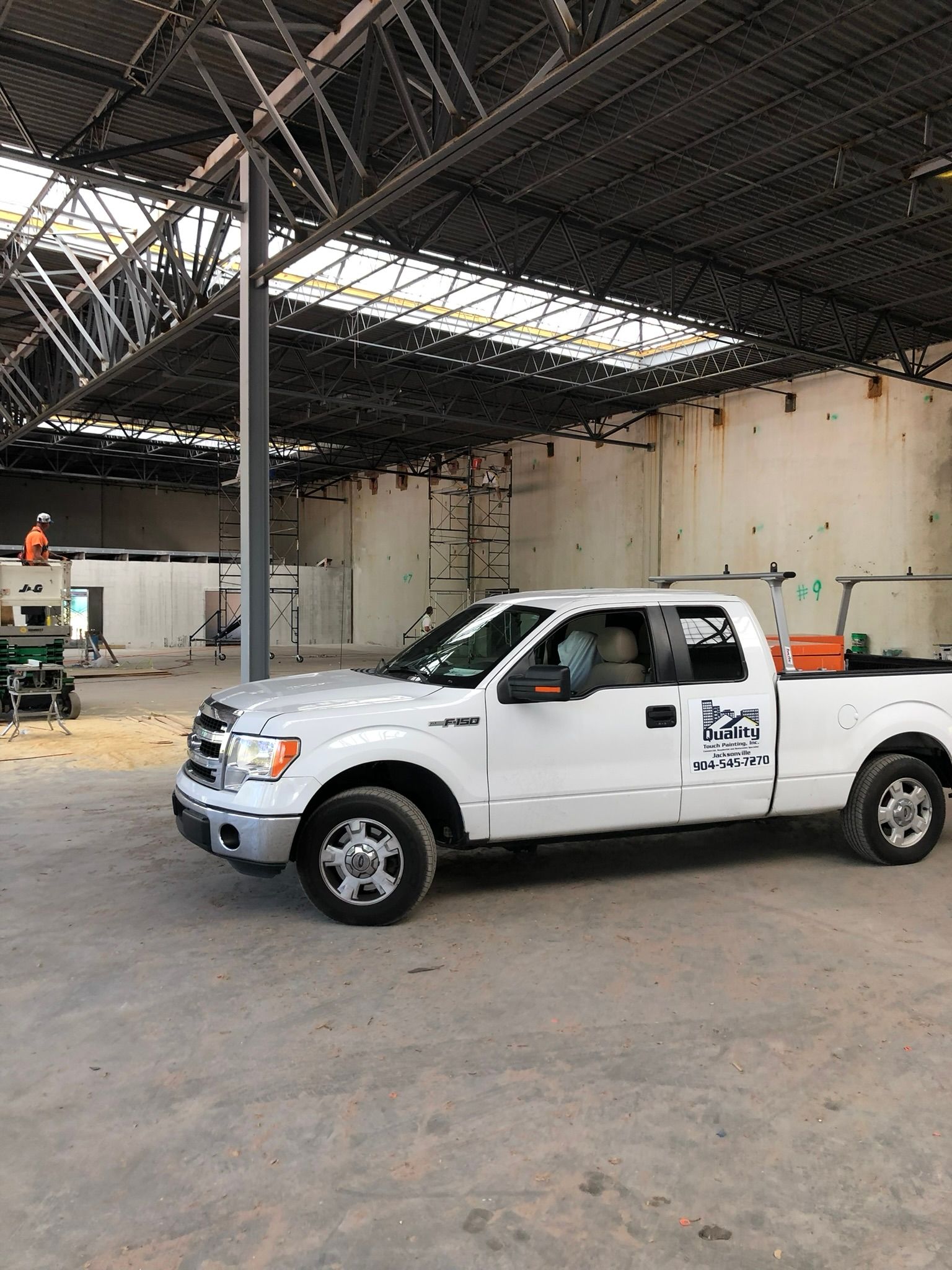 White pickup truck parked inside a building under construction; visible steel beams overhead.