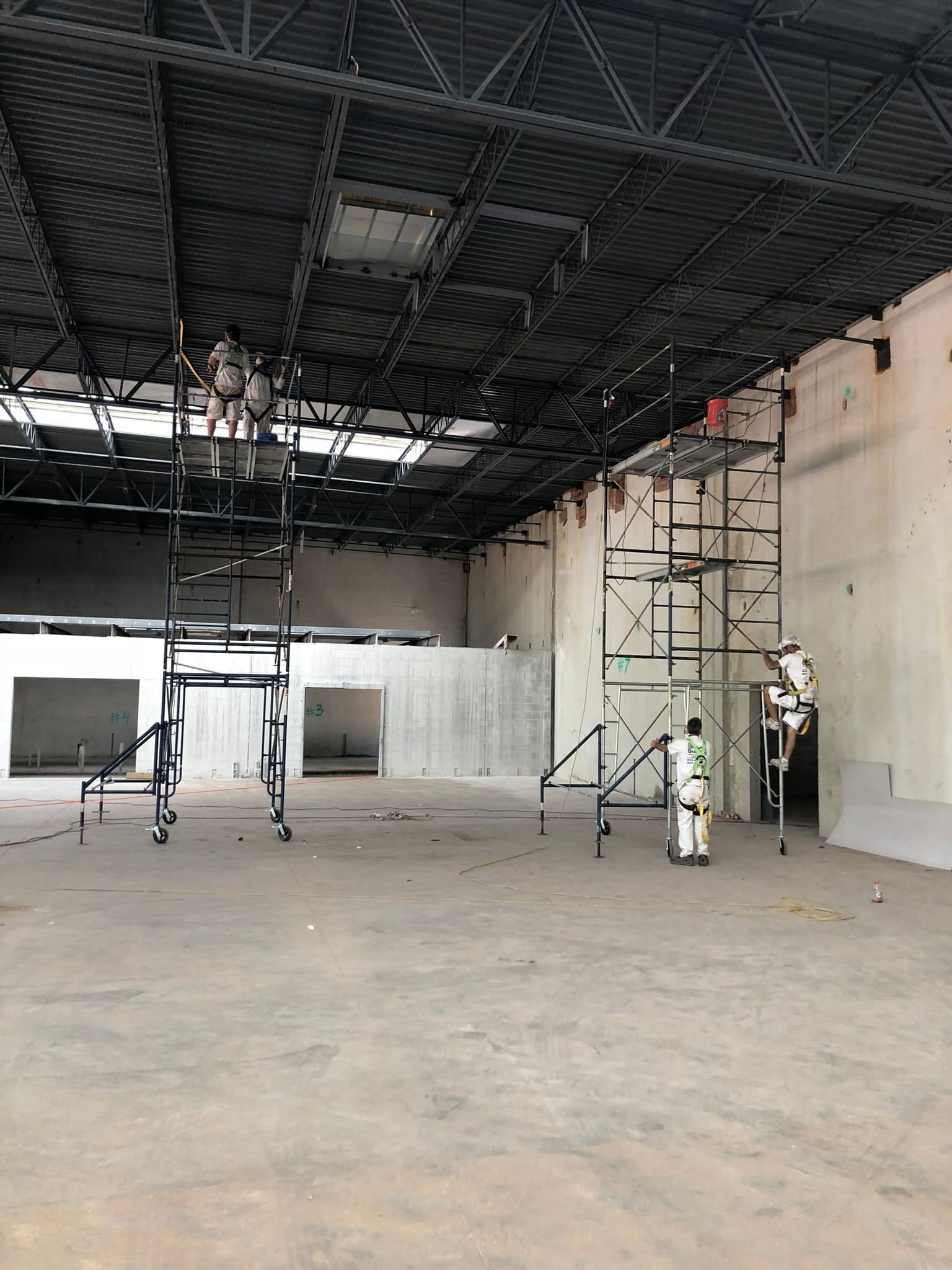 A large, empty warehouse under construction. Scaffoldings and a worker in white protective gear are visible.