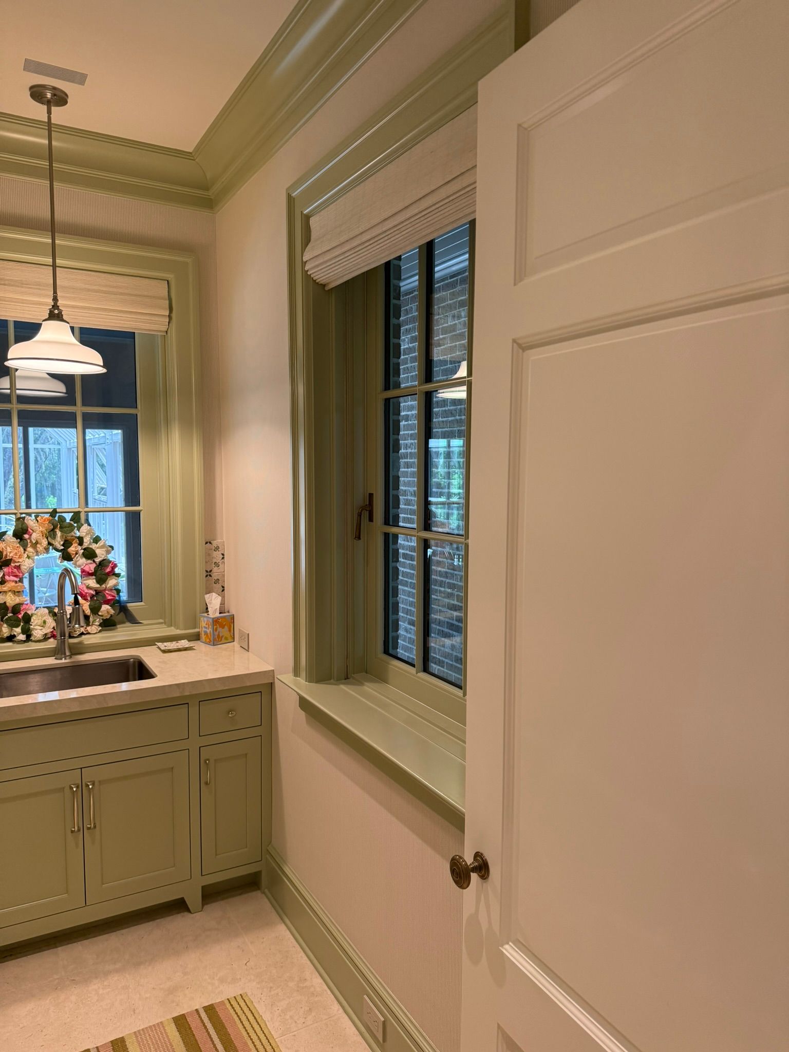 A light green kitchen with white walls, cabinets and trim. A window with a blind is visible.