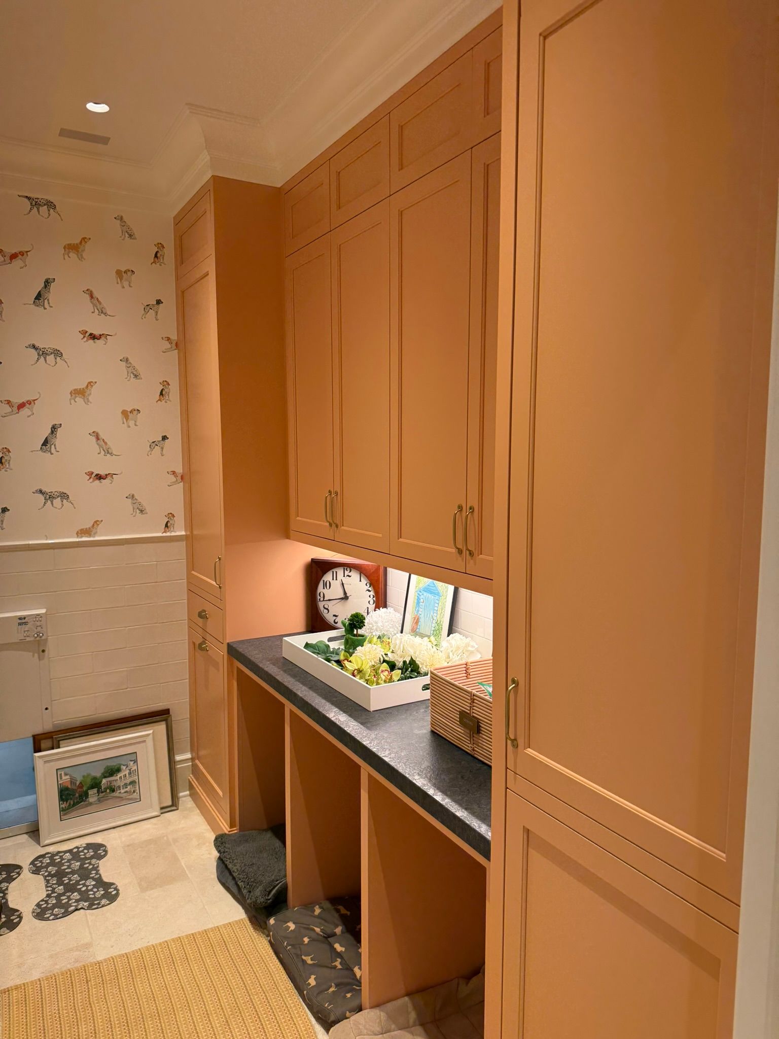 Peach-colored cabinetry in a laundry room with dog-themed wallpaper and a black countertop.