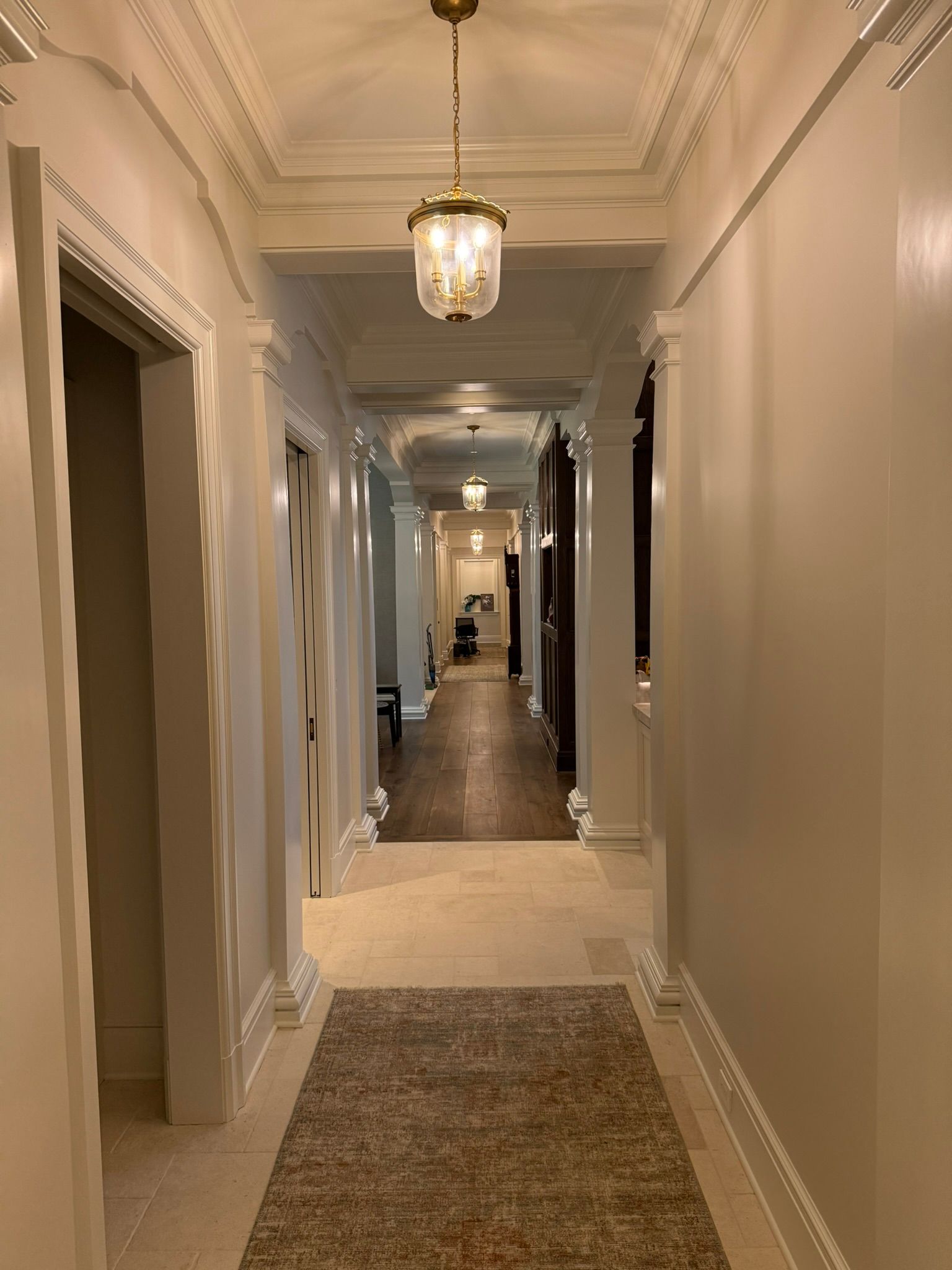 Long, bright hallway with decorative columns, light fixtures, and a patterned rug.