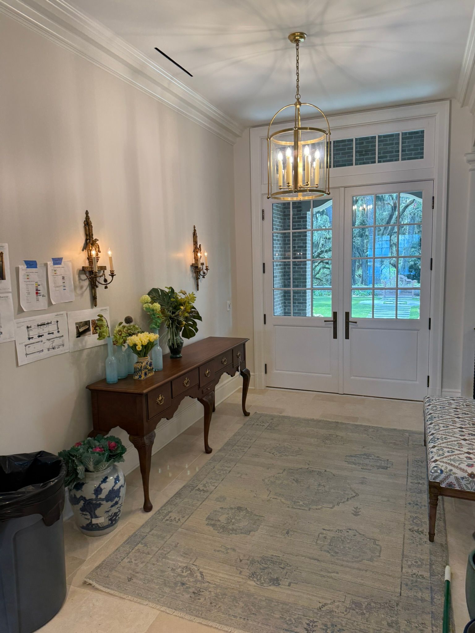 Entryway with wood console, antique rug, and French doors. Light fixtures, wall sconces, and flower arrangements present.