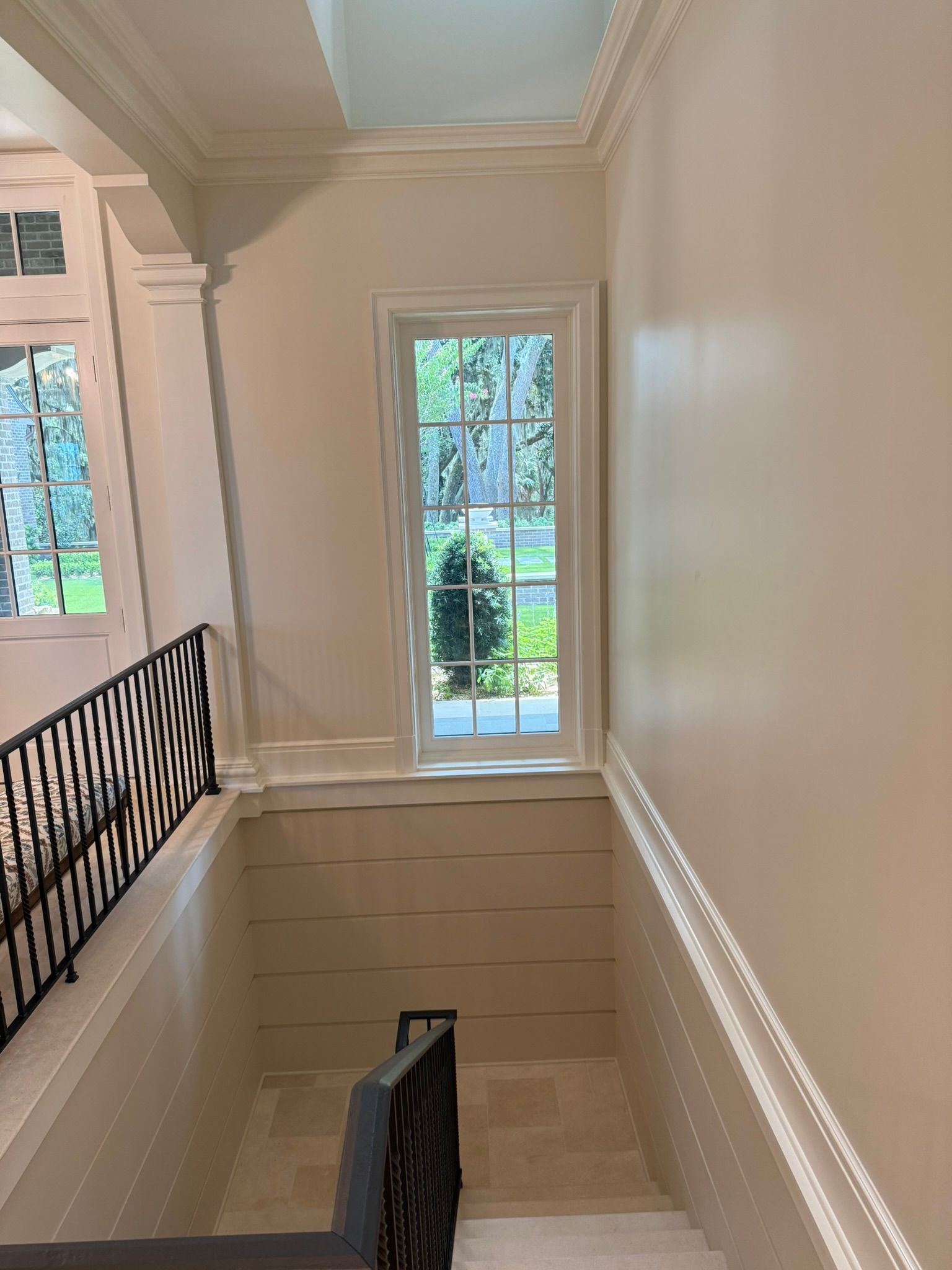 Interior staircase with a window at the top. White trim, beige walls, and black wrought iron railing.