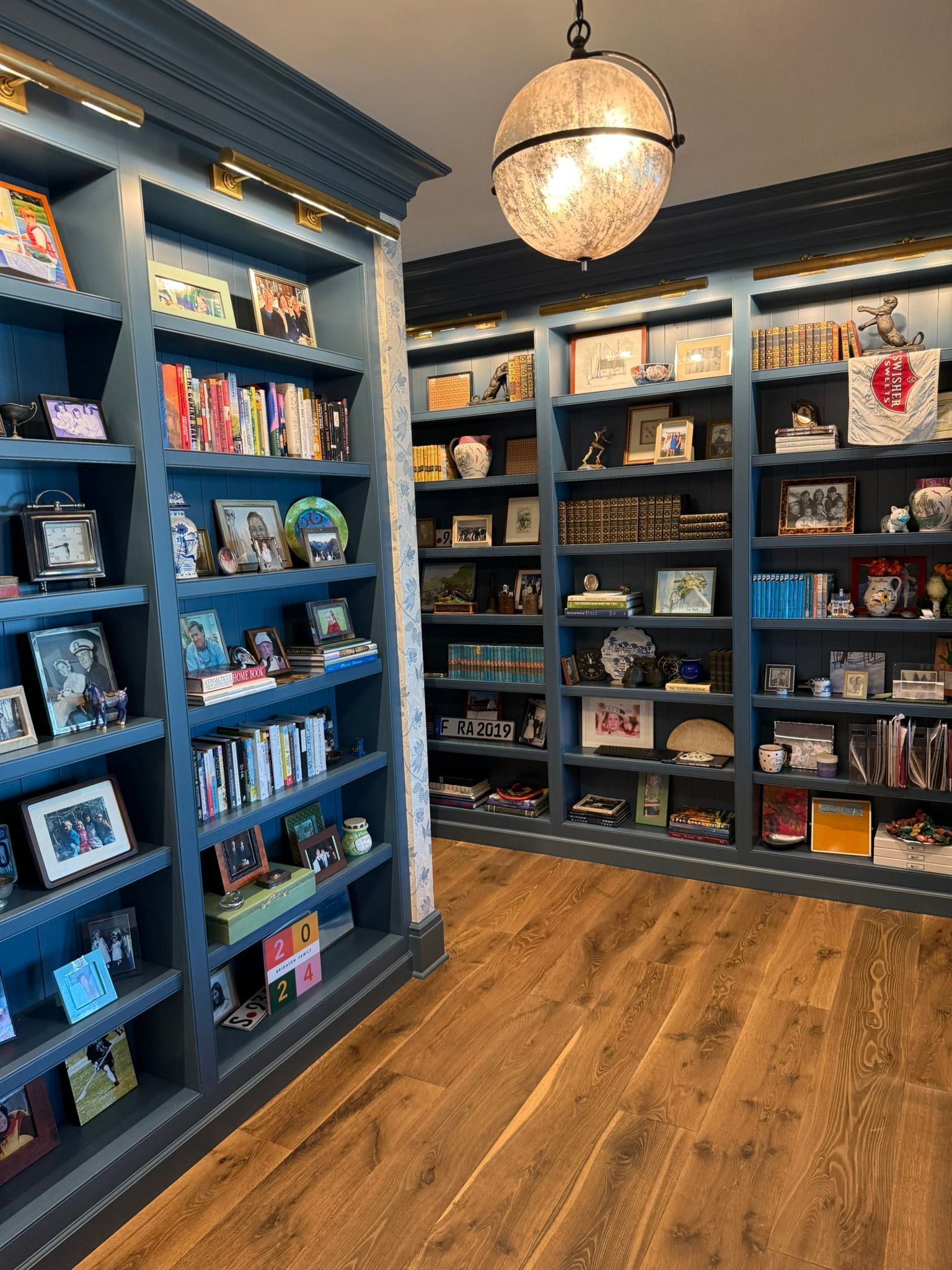 Blue bookshelves filled with books and decorations in a room with wood flooring, lit by a globe light.