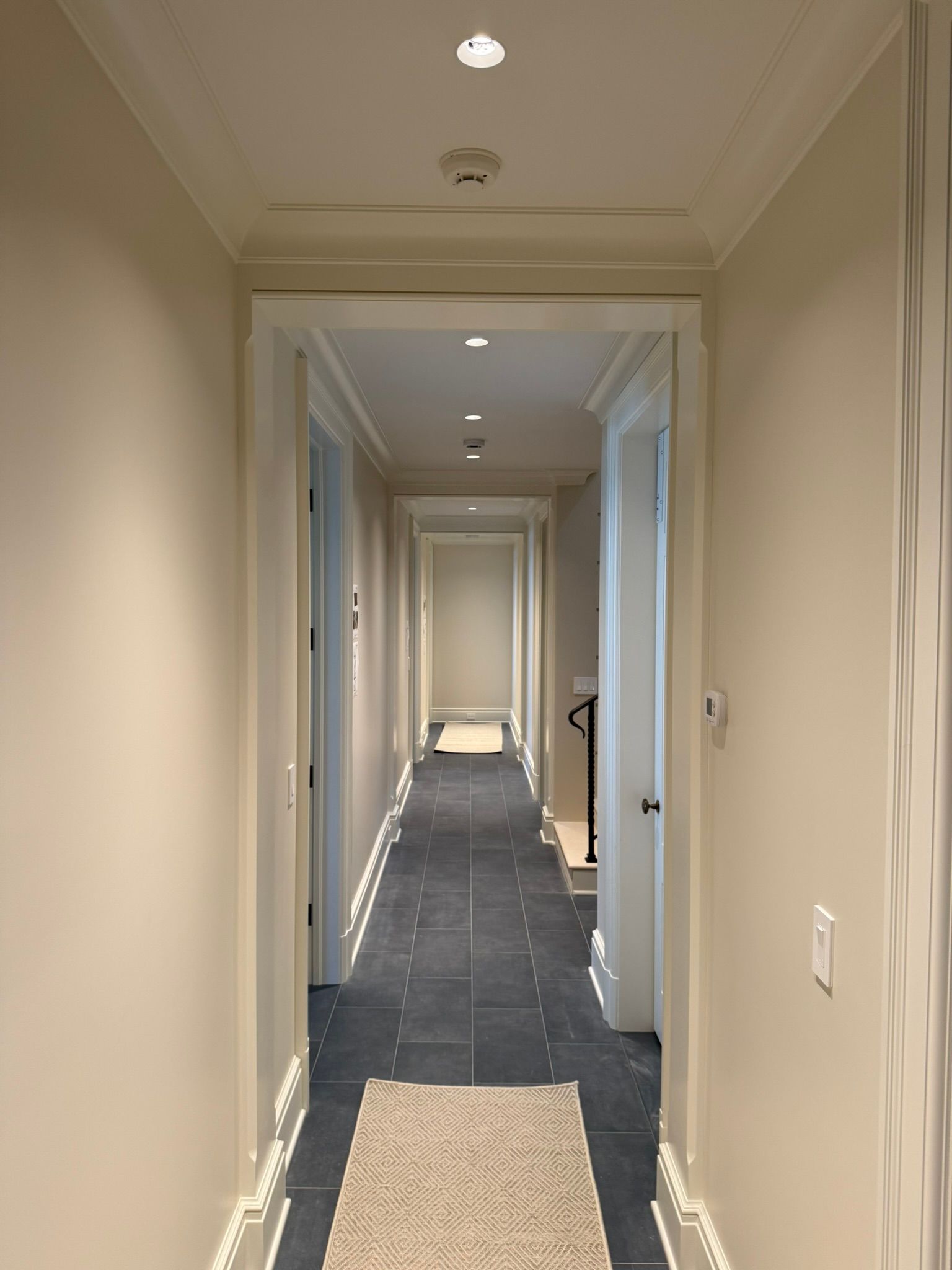 Long hallway with off-white walls, crown molding, dark blue floor, and recessed lighting.