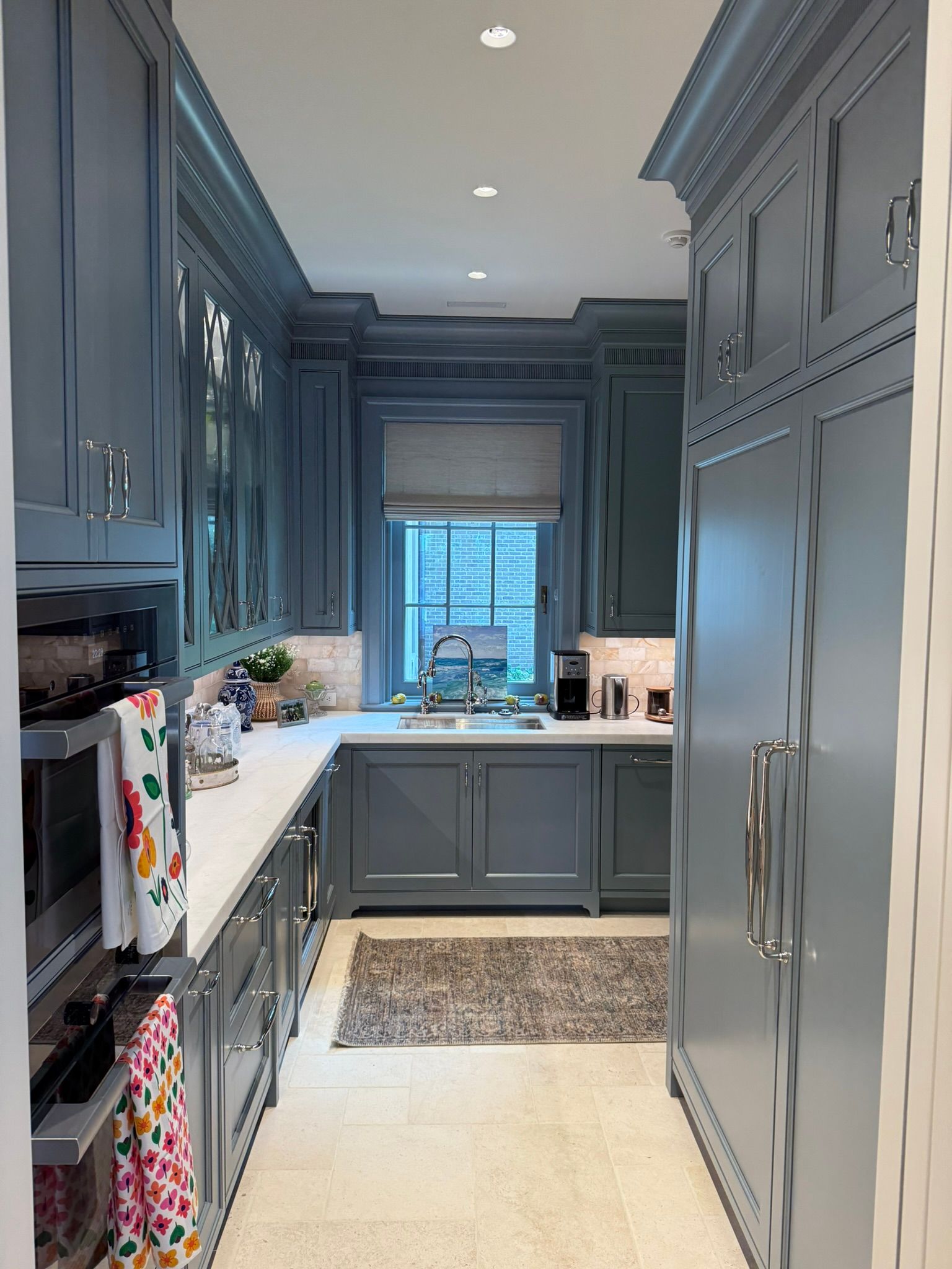 Narrow kitchen with blue cabinets, white countertops, window, and rug.