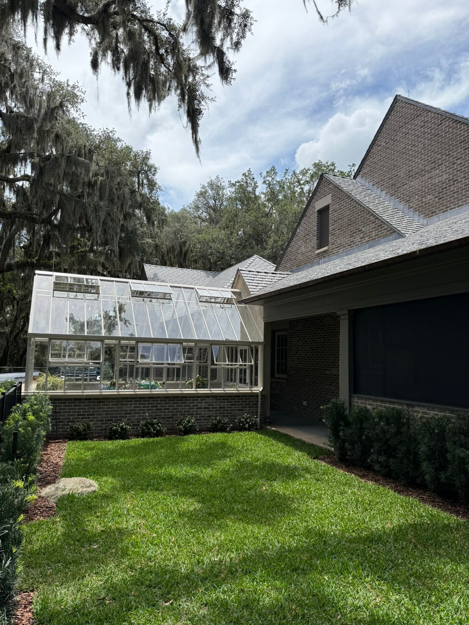 Greenhouse next to a house with metal roof; lush green lawn in front.