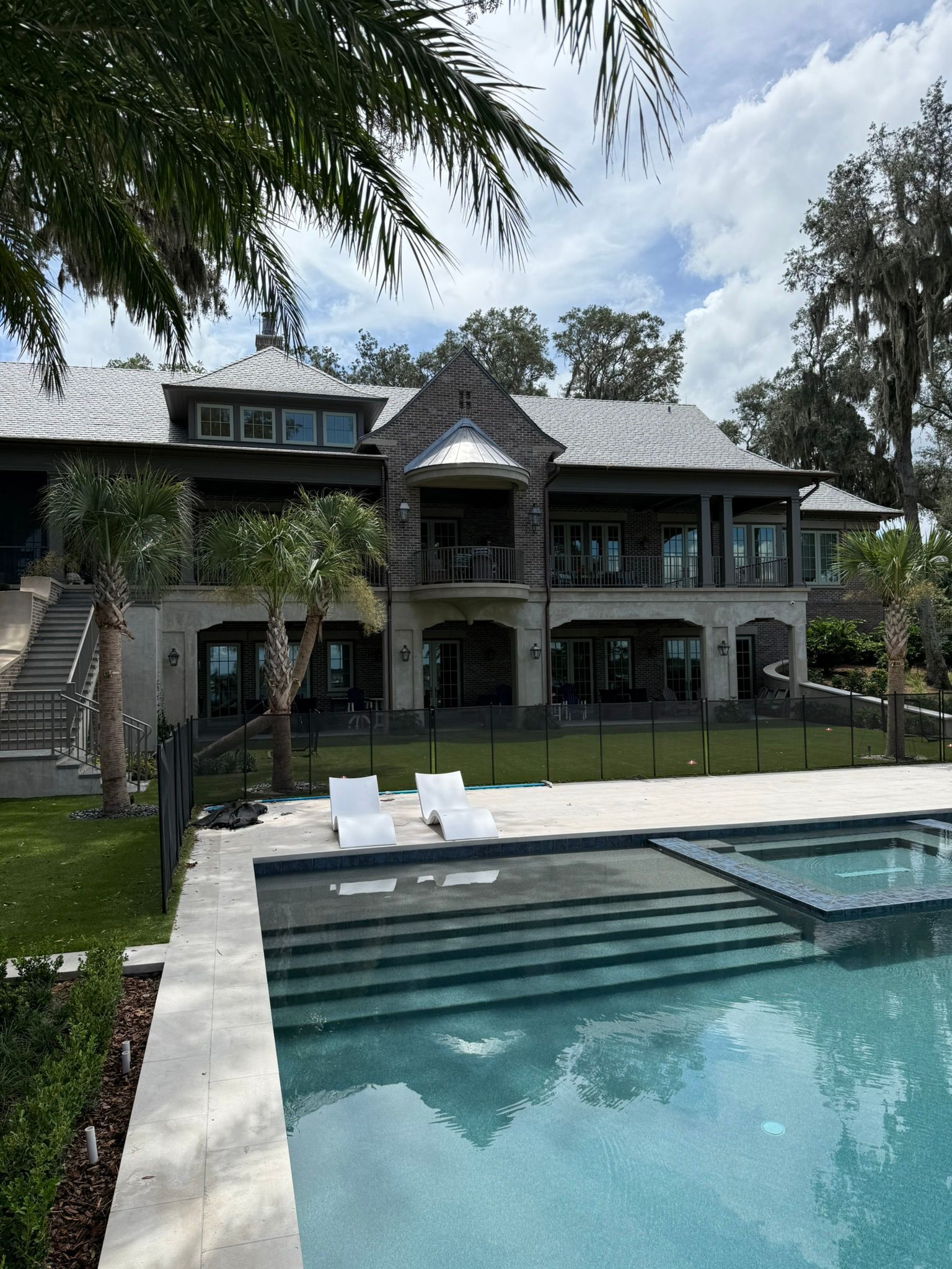 Luxurious waterfront home with a pool, palm trees, and clear blue sky.