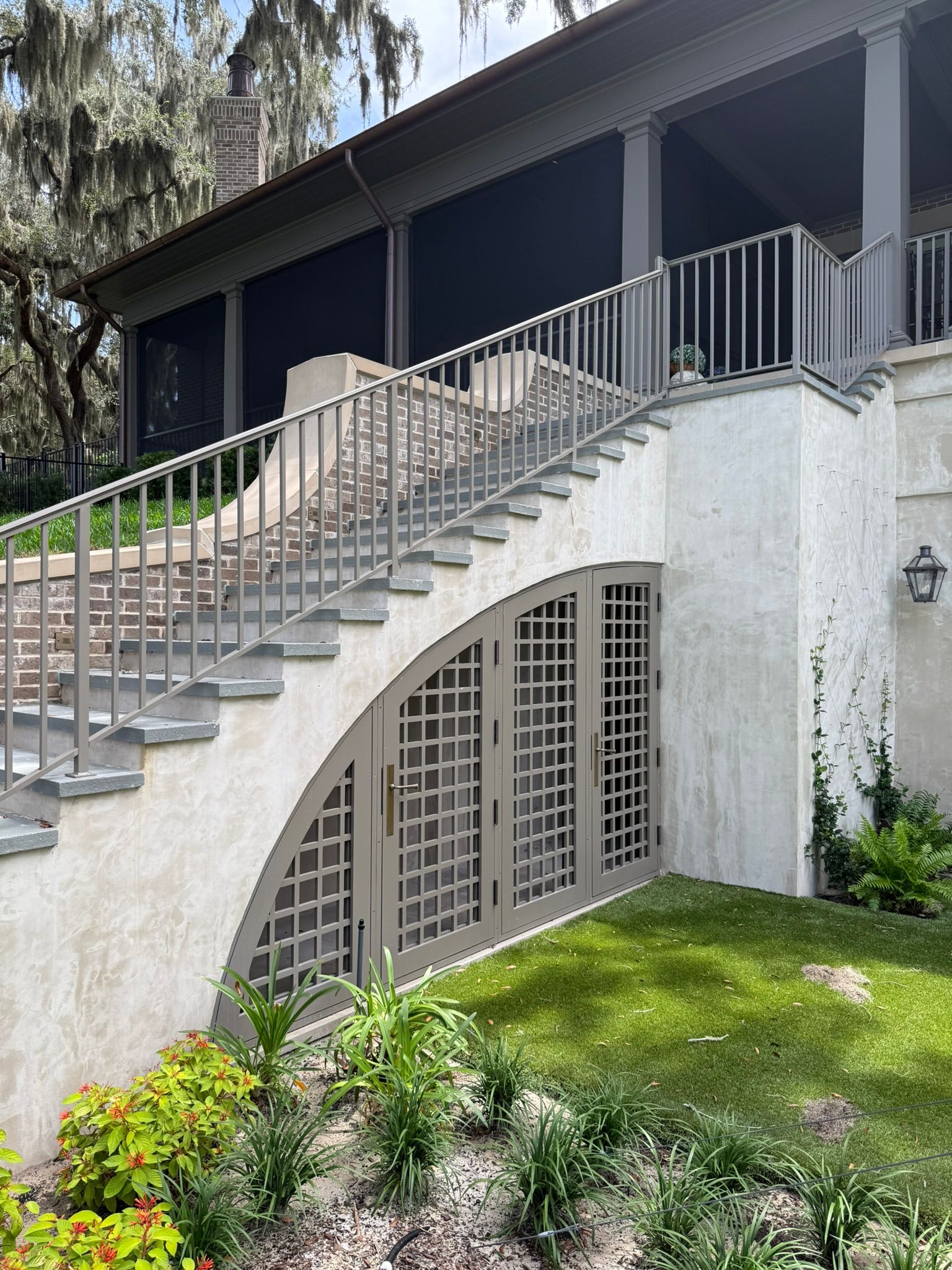 Exterior stairs leading up to a screened porch. Arched doors below, surrounded by stucco and landscaping.
