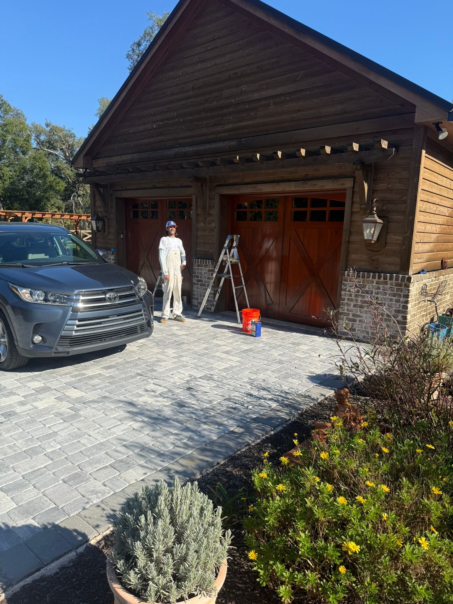 Person painting garage door; gray SUV parked on brick driveway.