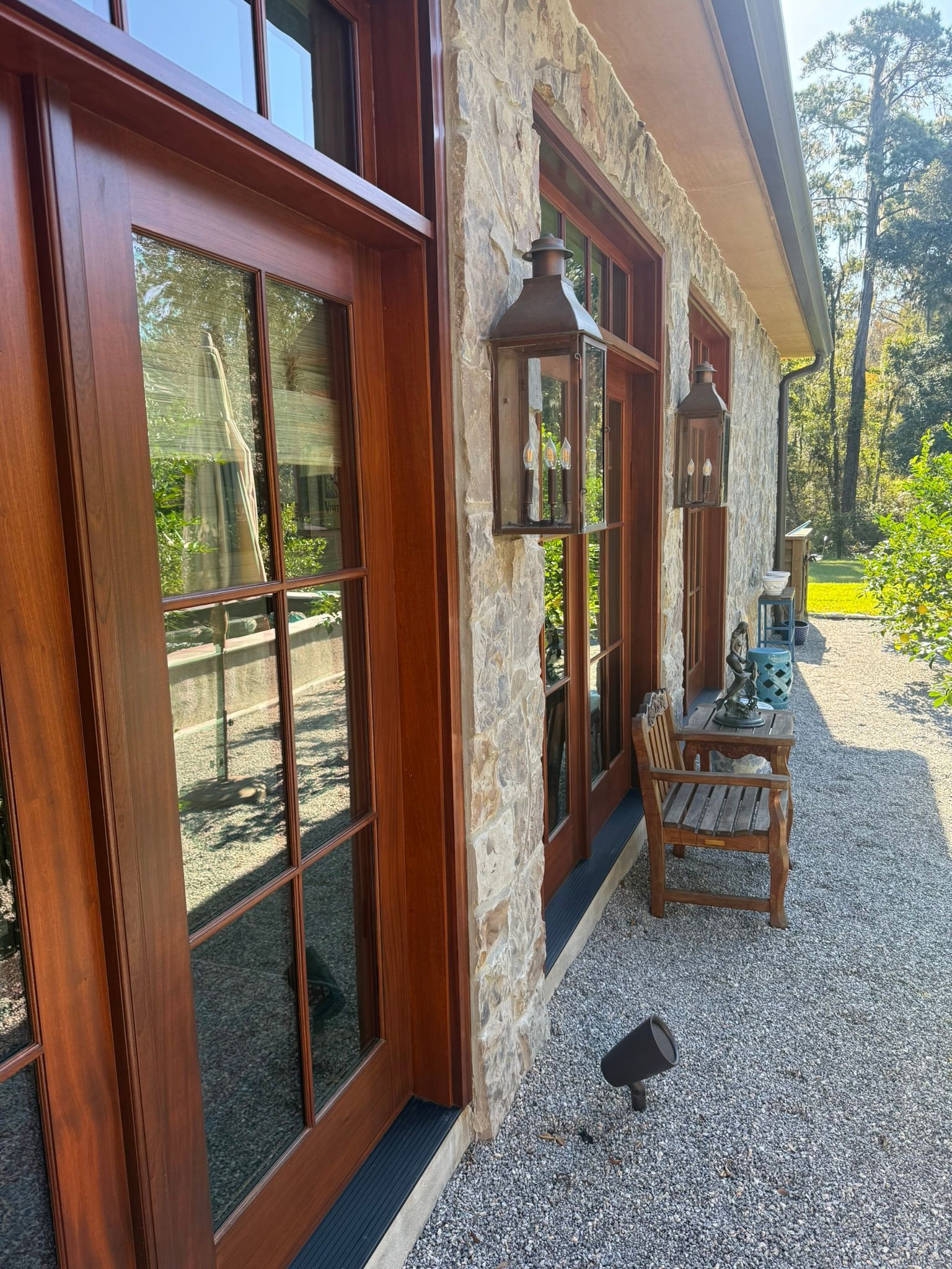 Exterior view of a building with brown doors, stone wall, and lanterns. A small chair sits by the wall.