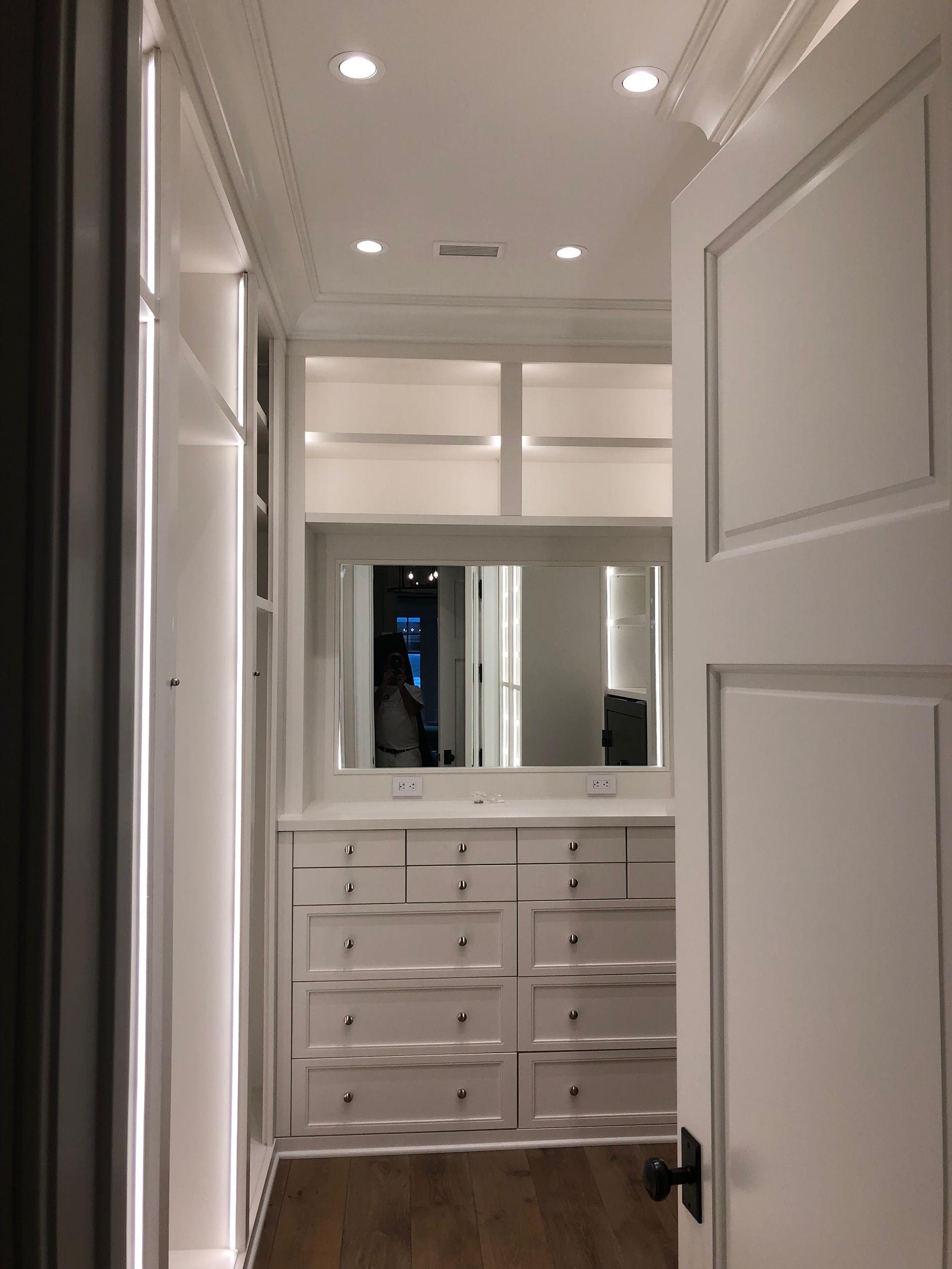 White walk-in closet with built-in drawers, shelves, and a large mirror; the door is slightly ajar.