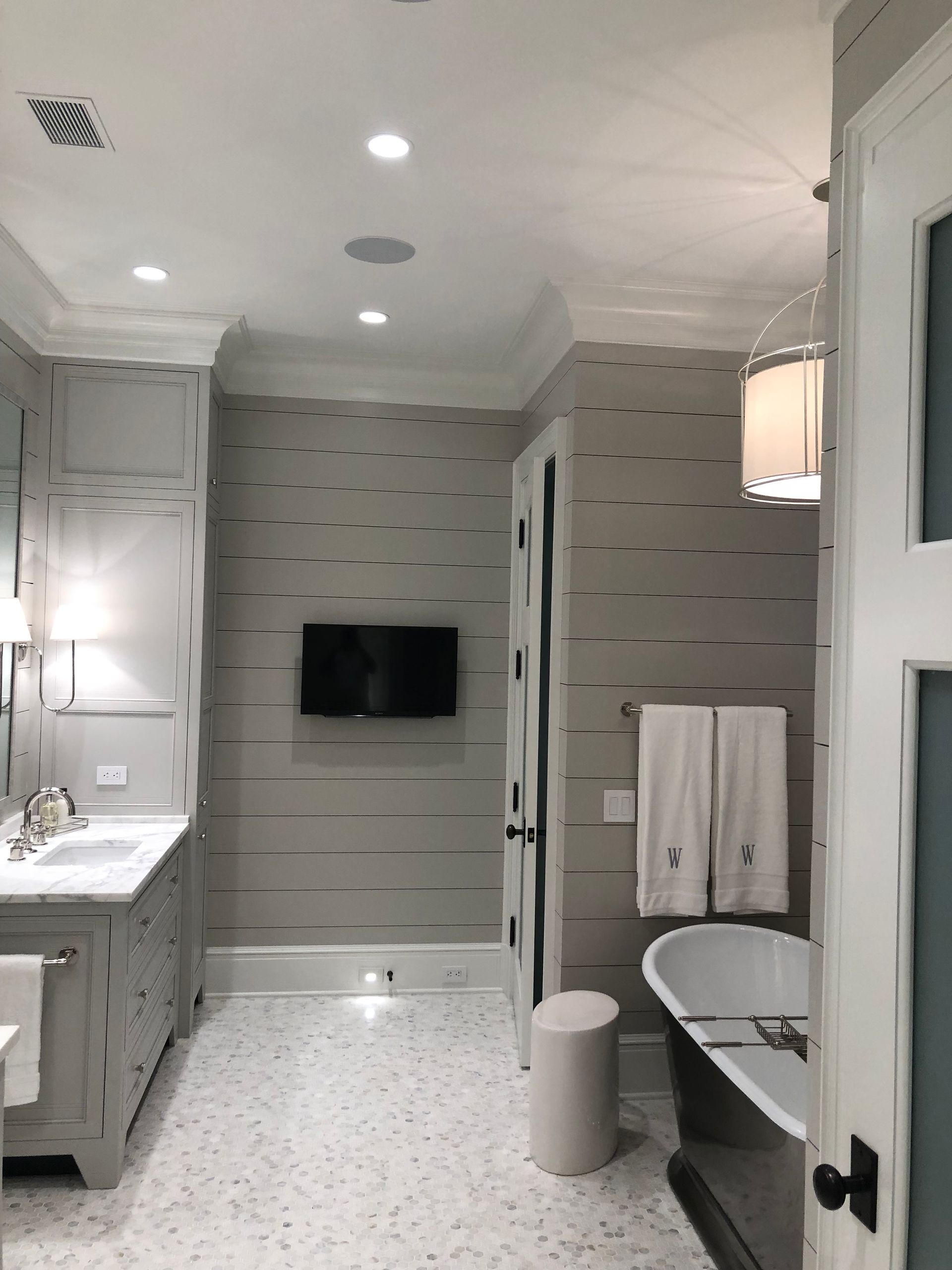 Elegant bathroom with gray wallpaper, a white bathtub, and a mounted TV.