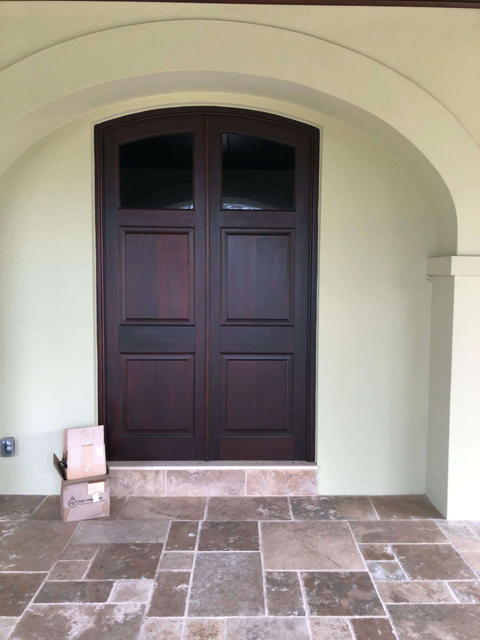 Dark wooden double doors under an arched entryway on a light green wall, with a stone floor.