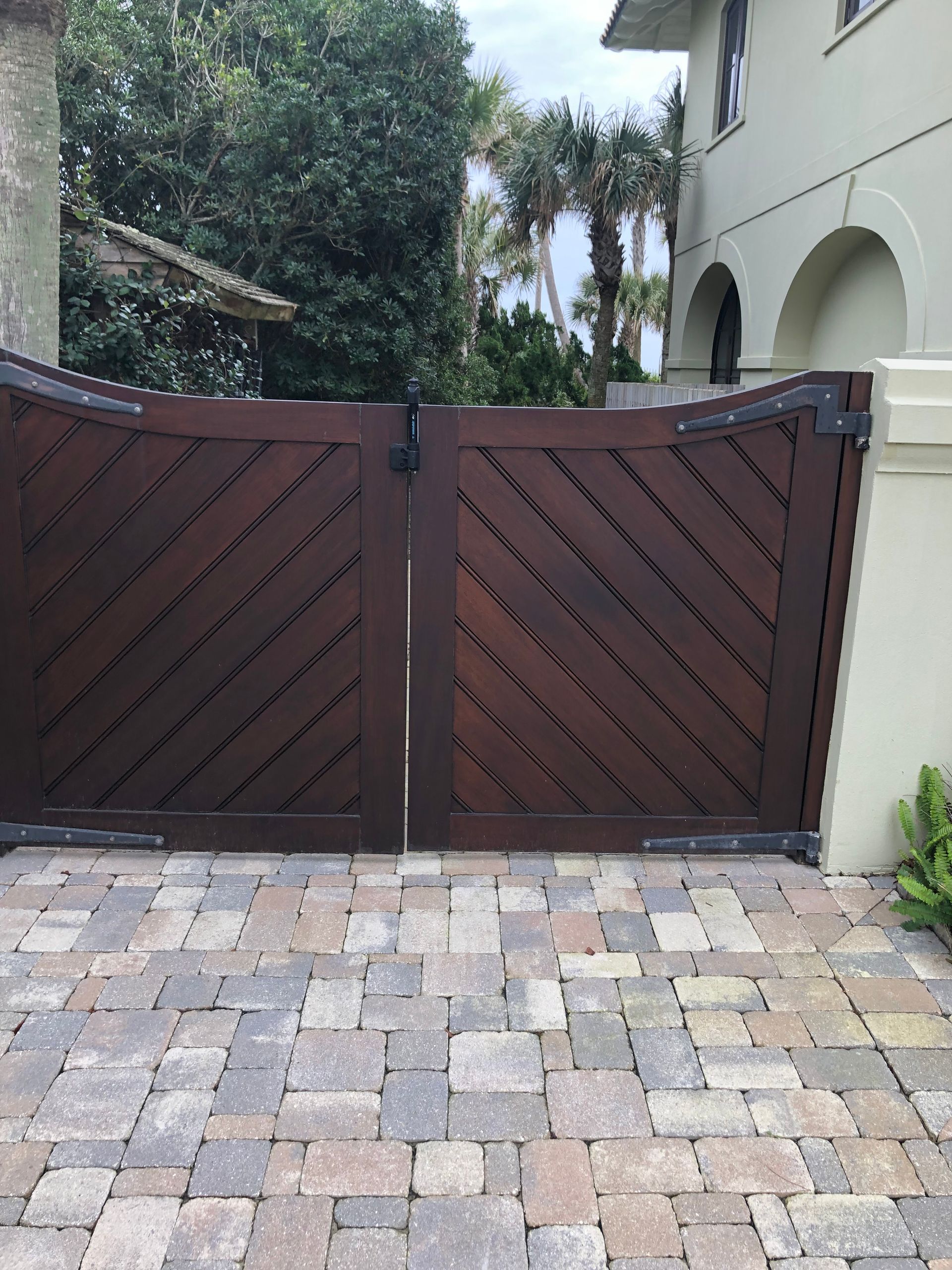 Dark wooden gate with diagonal planks, on a brick paved driveway.