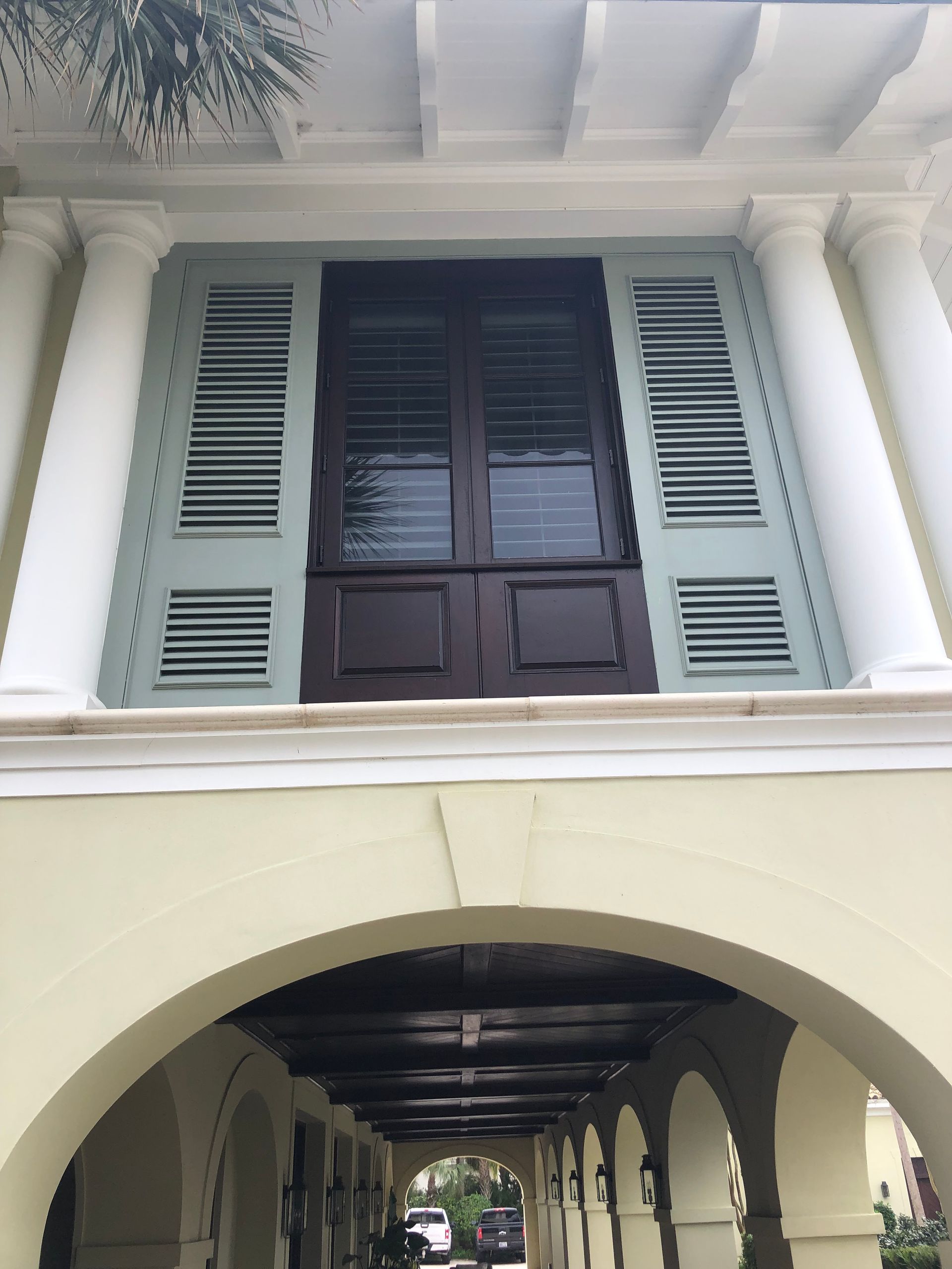 Building facade with arched colonnade below window with shutters and columns.
