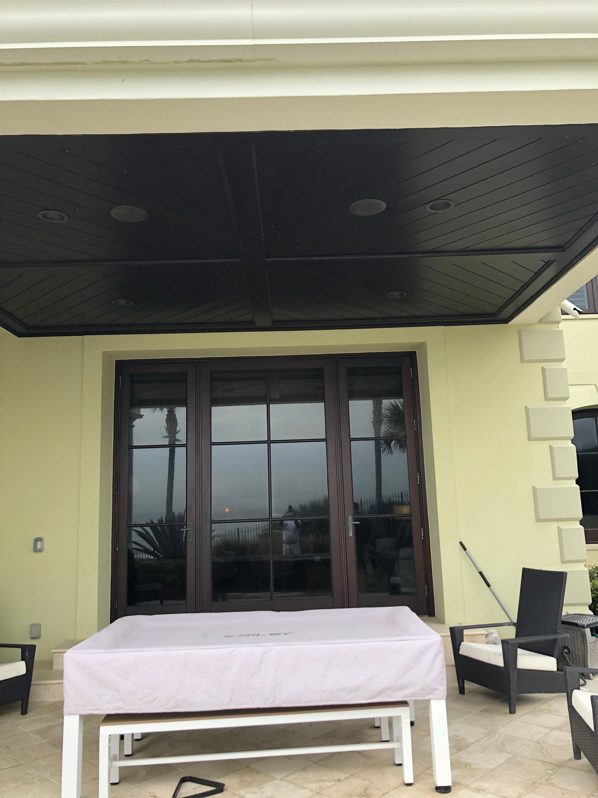 Outdoor covered patio with dark brown doors, a table, and seating. Black ceiling.