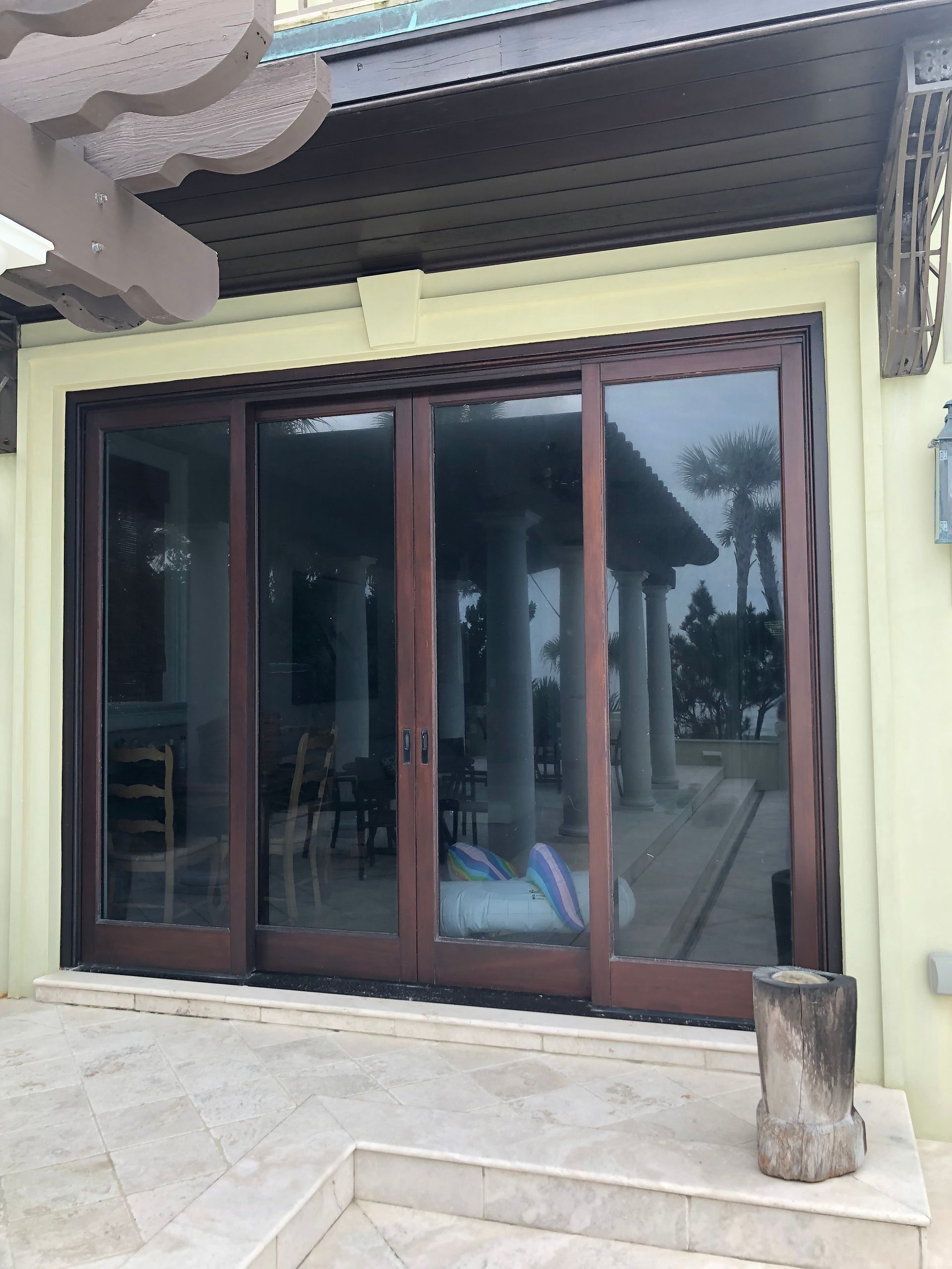 Wooden sliding glass doors on a light yellow building, reflecting an outdoor seating area.