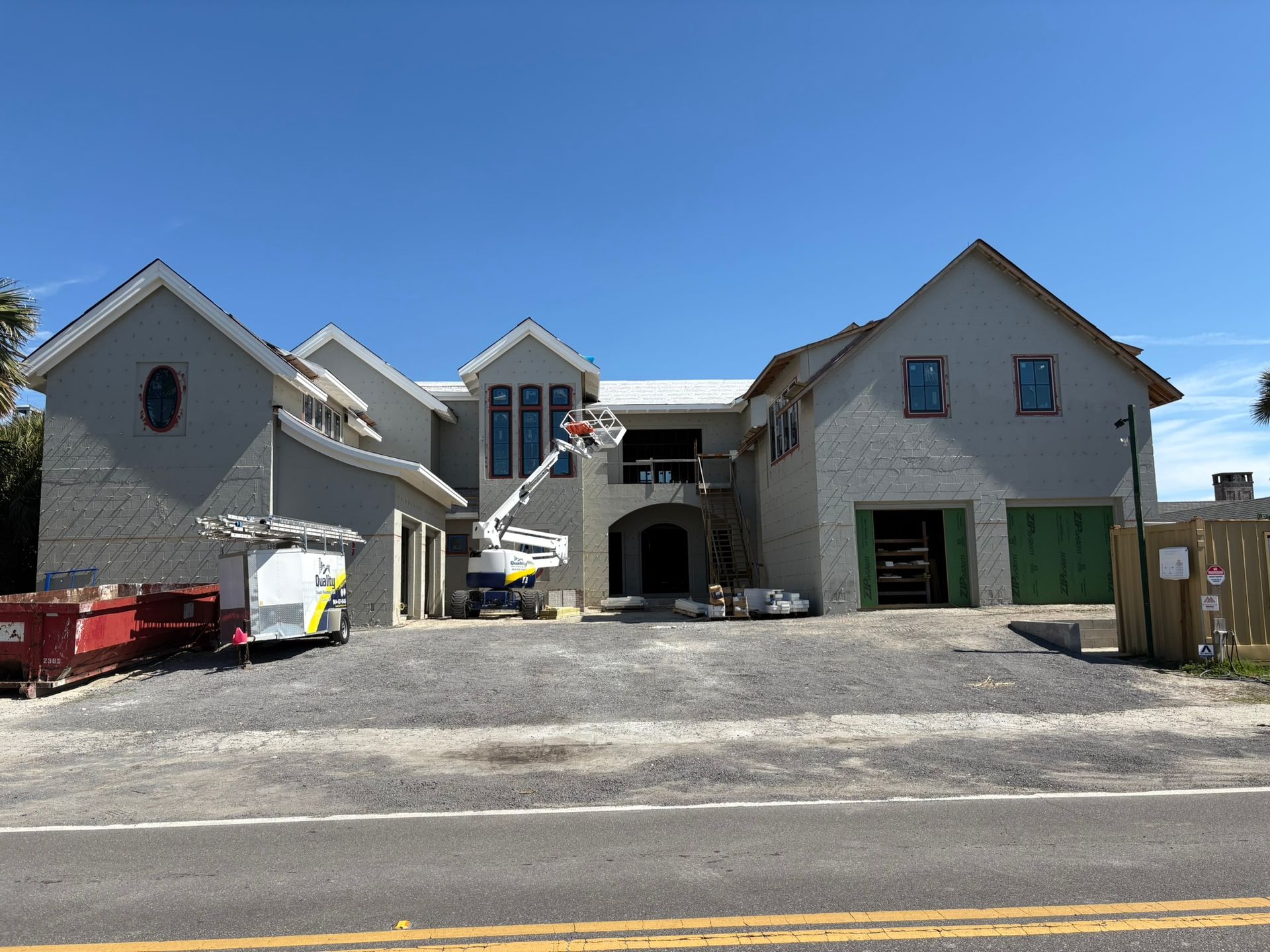 House under construction, gray brick, blue sky, lift in use, gravel driveway.