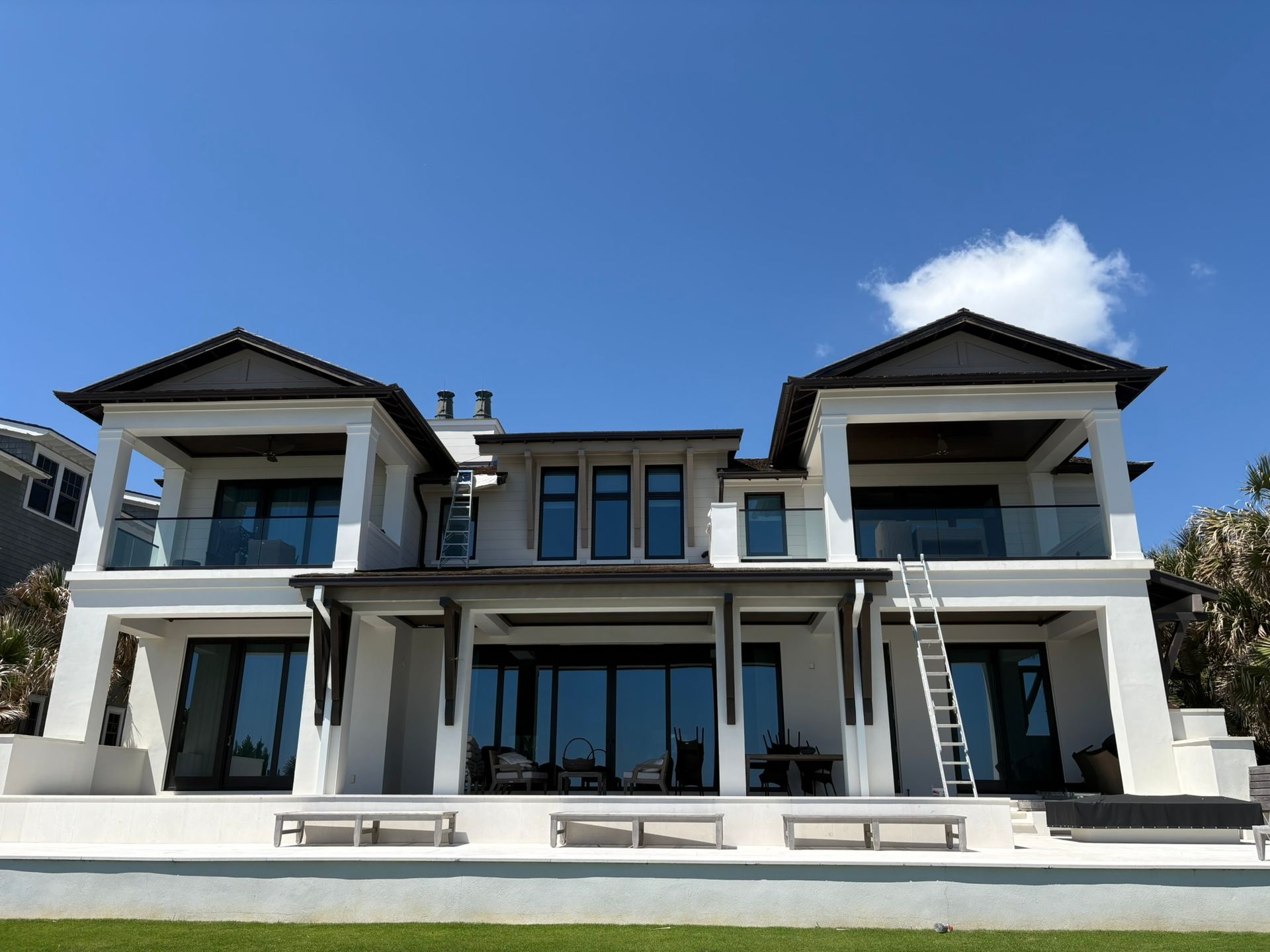 White two-story house with black trim and glass balconies under a bright blue sky.