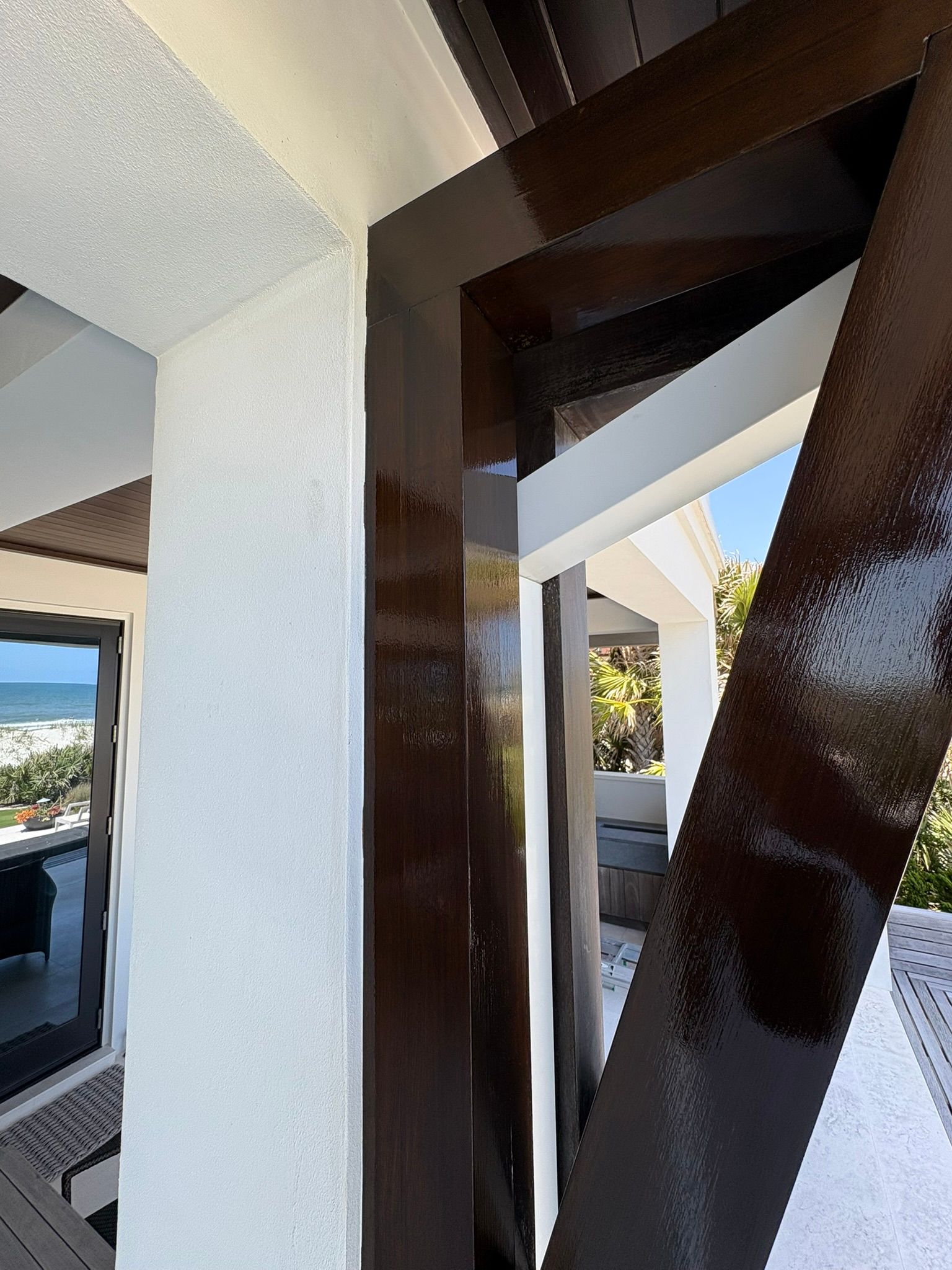 Exterior view: Brown, glossy beams against white stucco and a coastal landscape.