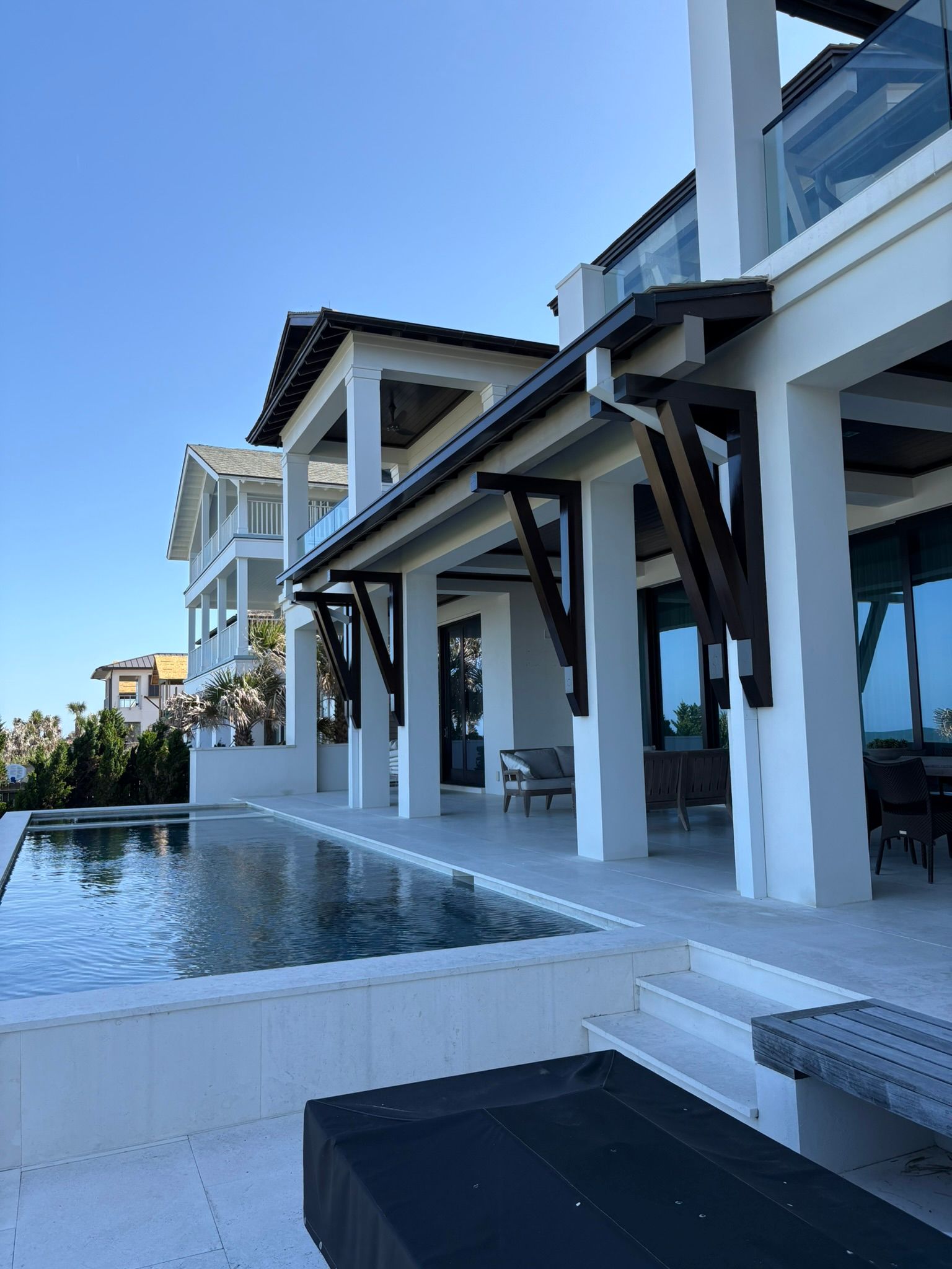 A white, multi-story beach house with a pool and a blue sky.