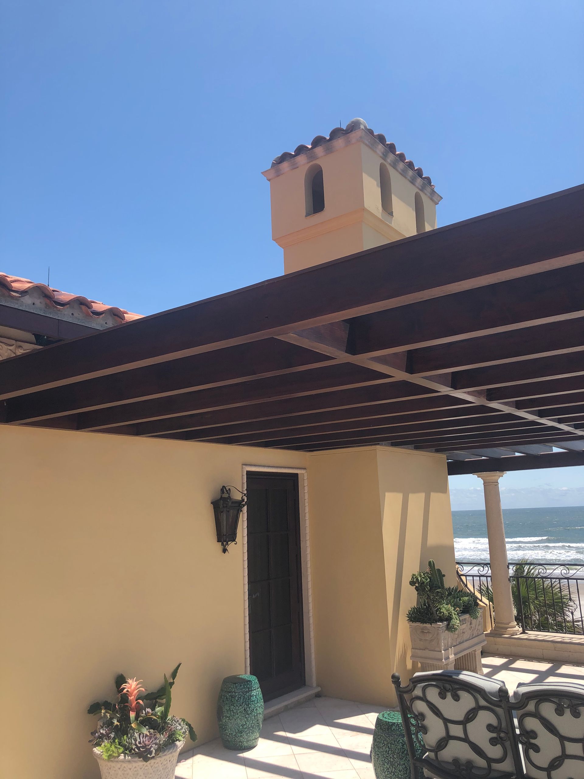 Terrace with pergola, yellow stucco walls, tower, and ocean view on a sunny day.