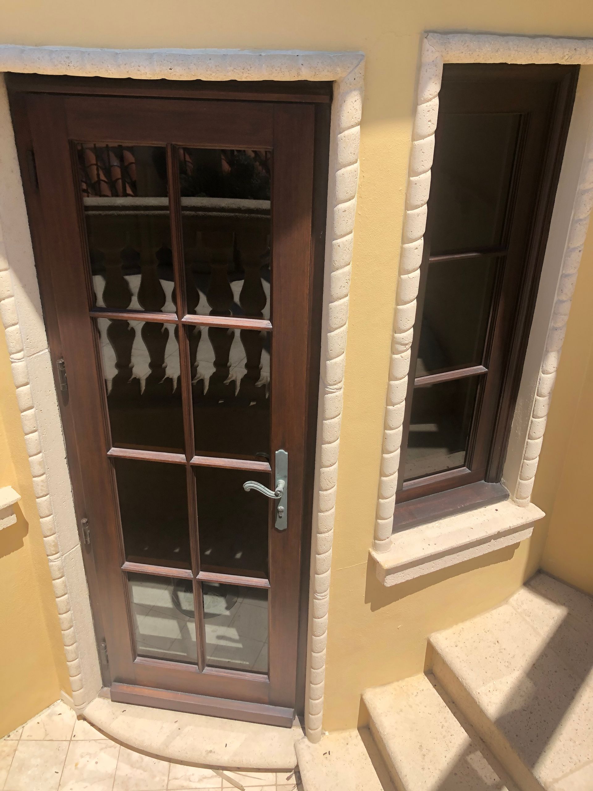 Wooden door and window with light stone trim on yellow stucco wall.