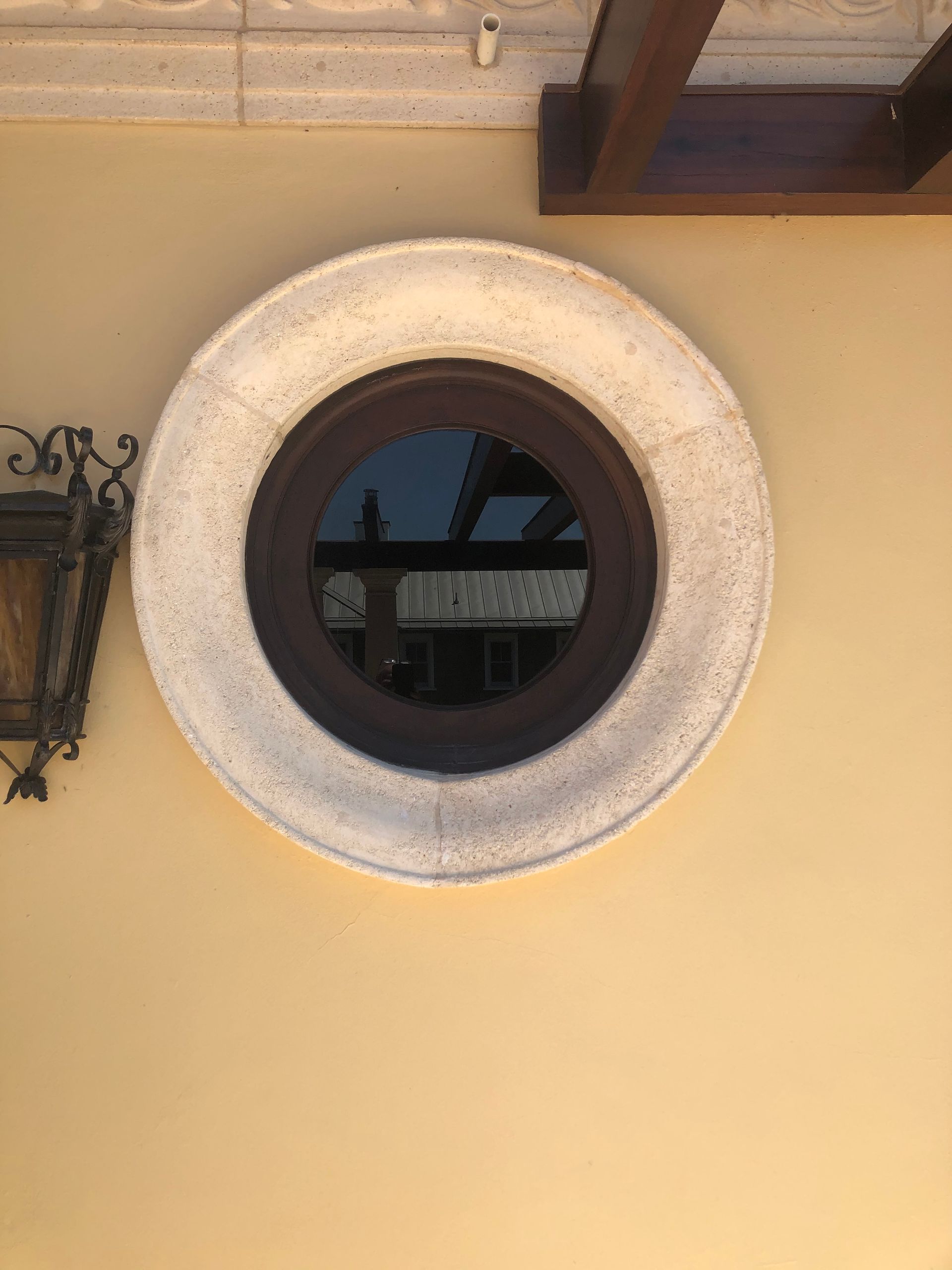 Round window with a light stone frame in a yellow wall.