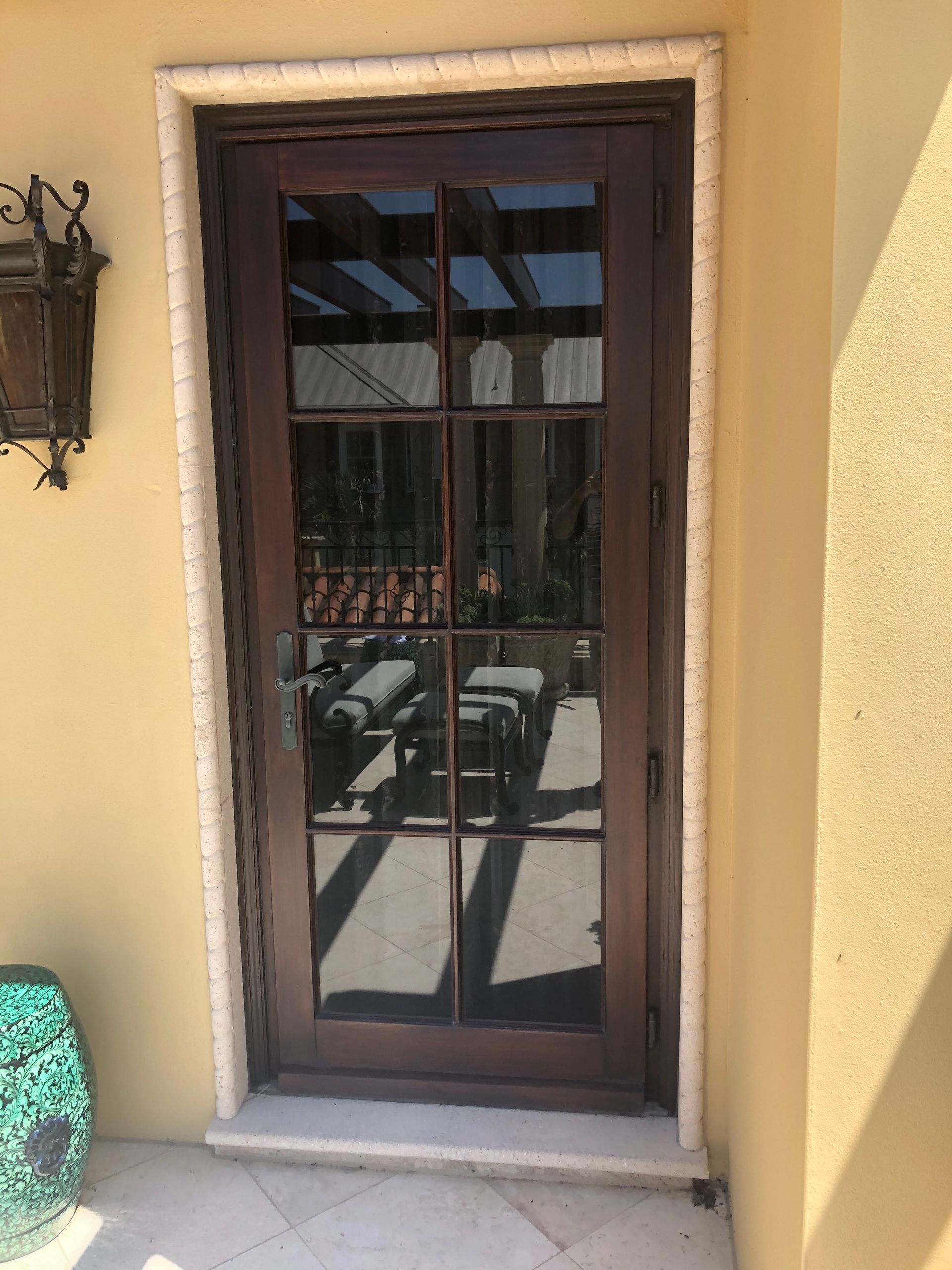 Dark wooden door with glass panels set in a beige stucco wall with a decorative white trim.