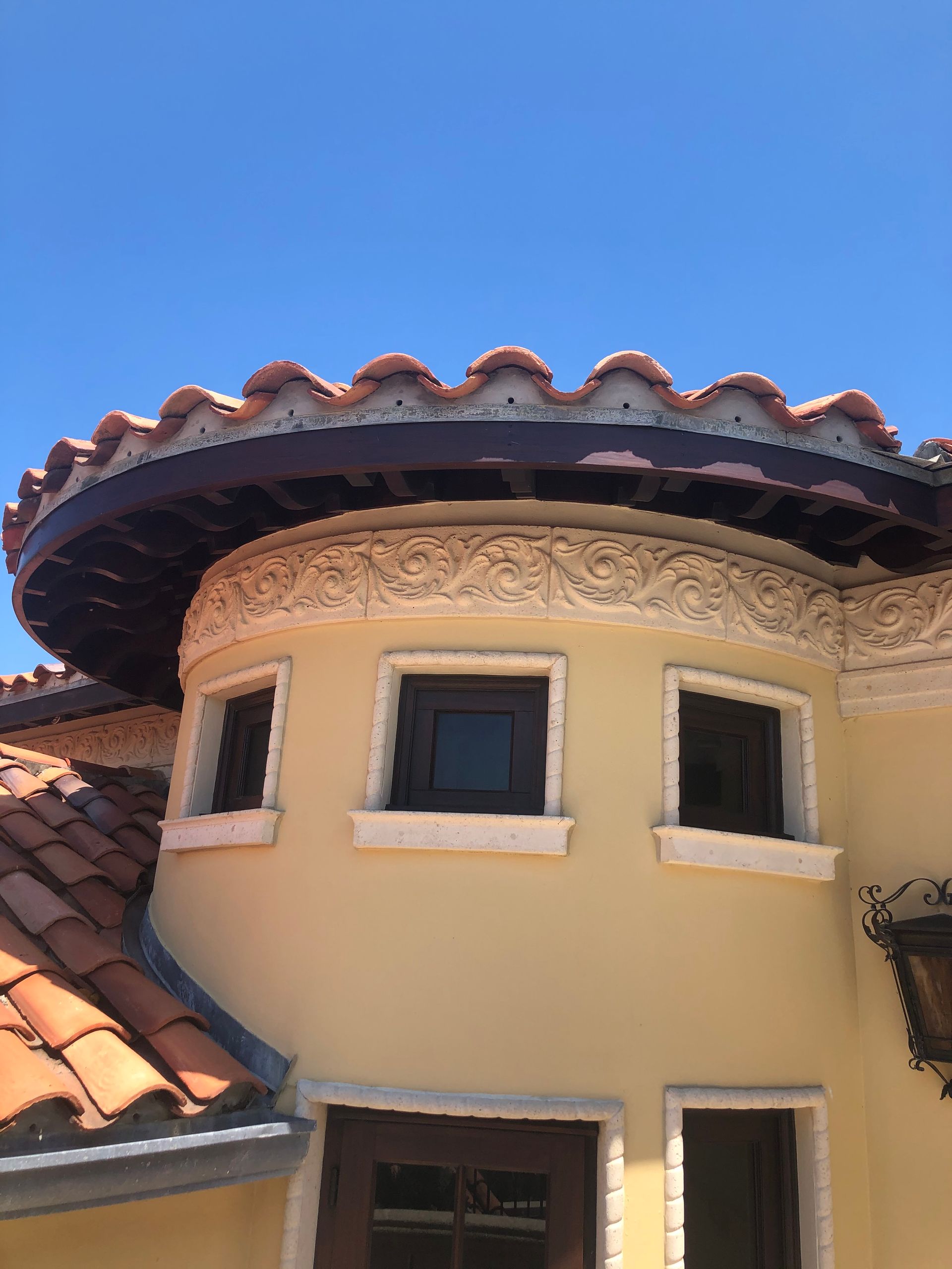 Curved building exterior with terracotta roof tiles, light-colored walls, and decorative trim, under a clear blue sky.