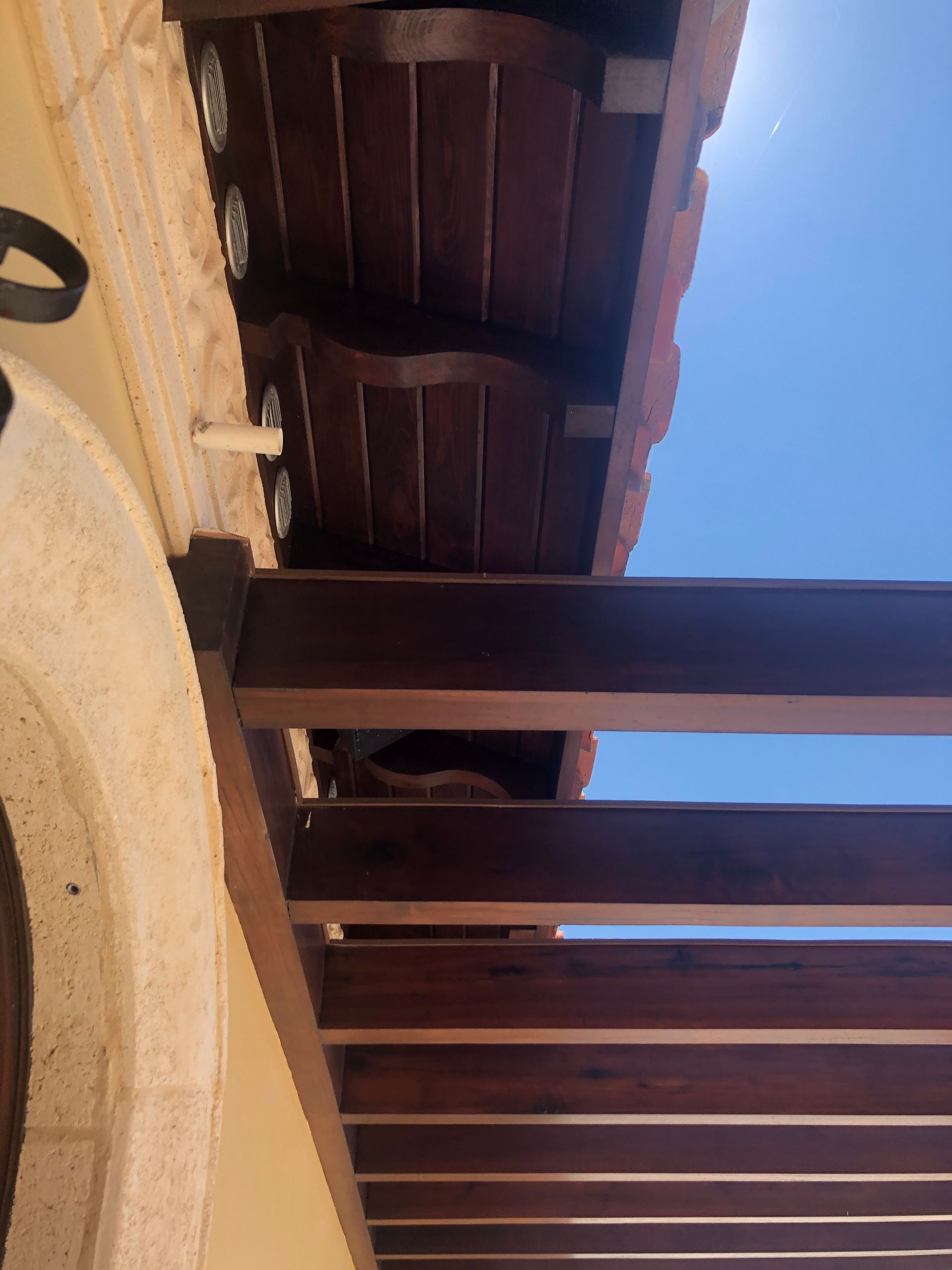Wooden pergola with brown beams and roof slats against a blue sky.